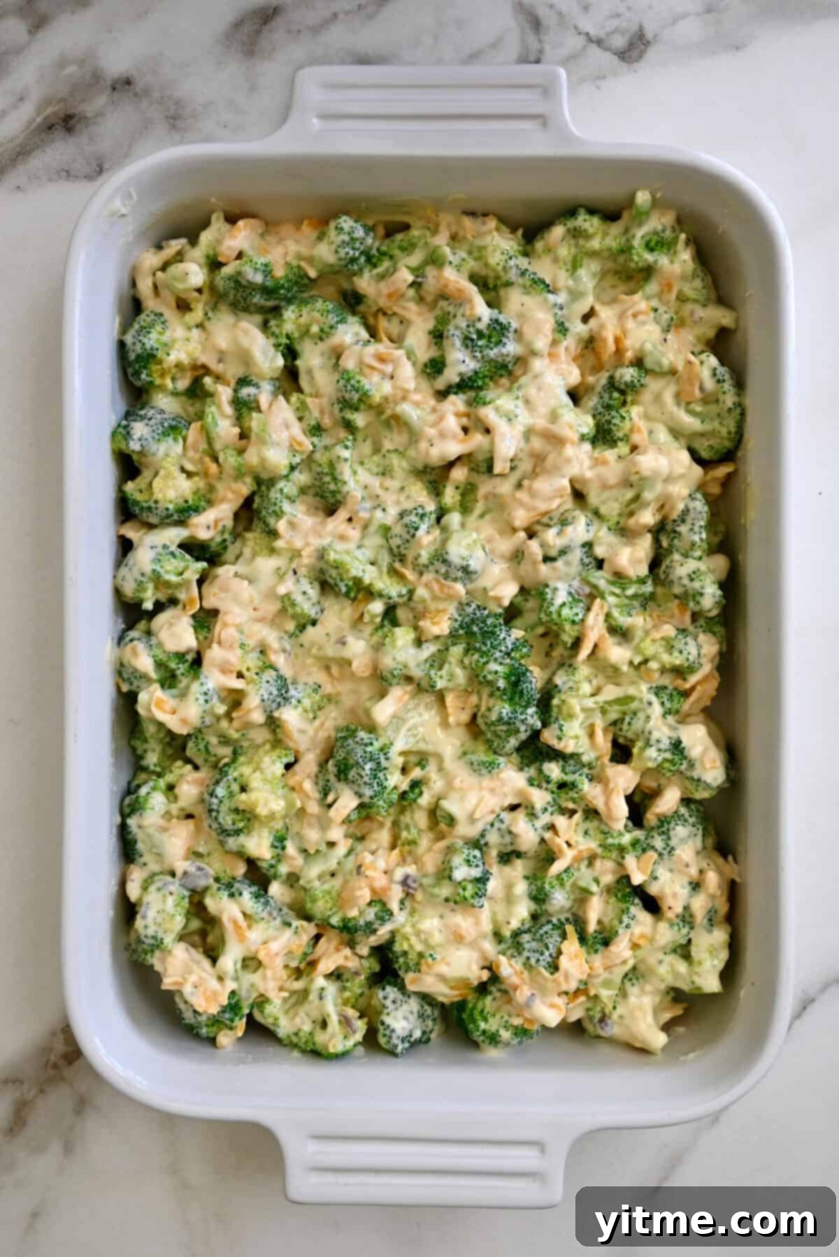 Unbaked broccoli cheddar cheese casserole in a white 9x13 baking dish. Ready to bake in the oven.