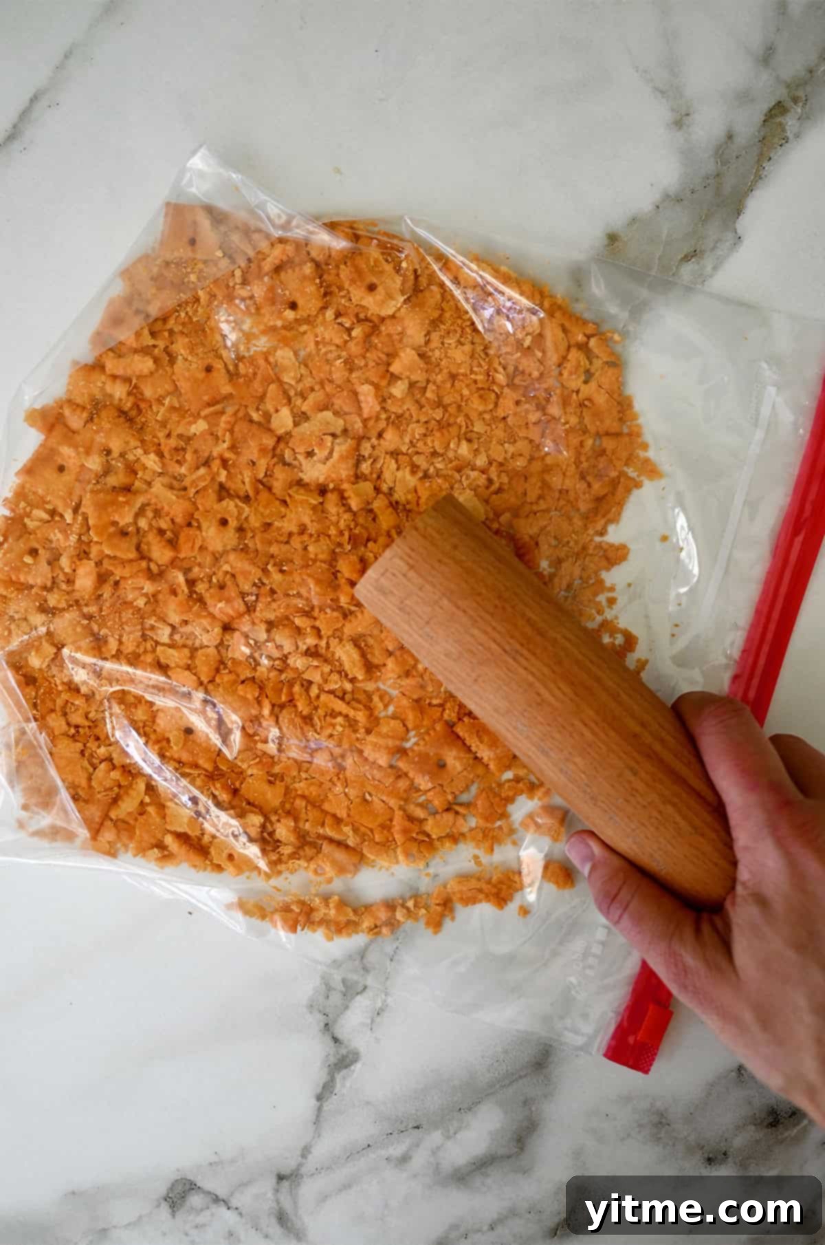Crushing cheese crackers in a sealed plastic bag with a rolling pin. Preparing the cracker topping.