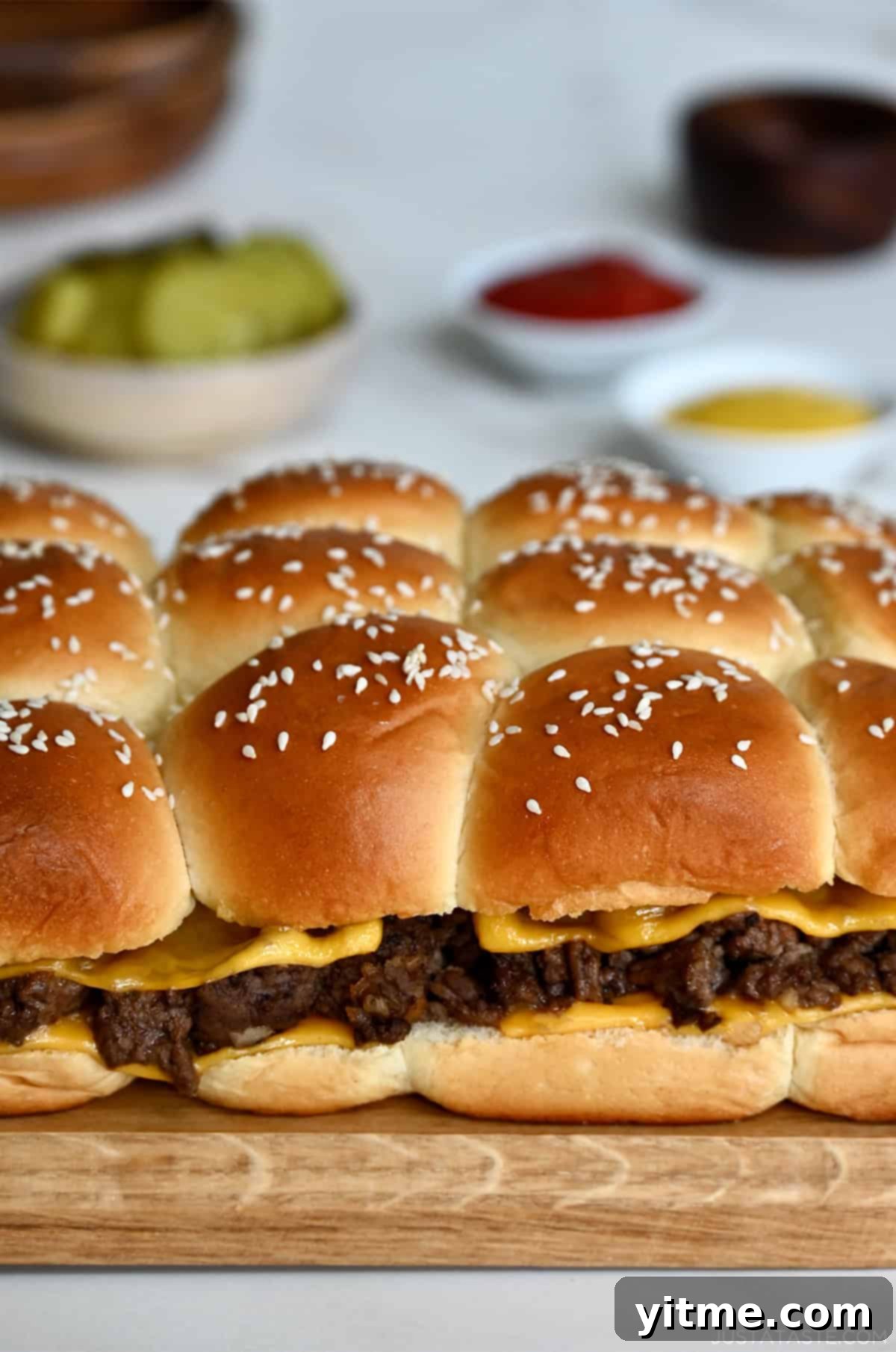 Baked cheeseburger sliders on sweet Hawaiian rolls topped with sesame seeds, ready to be pulled apart and enjoyed.