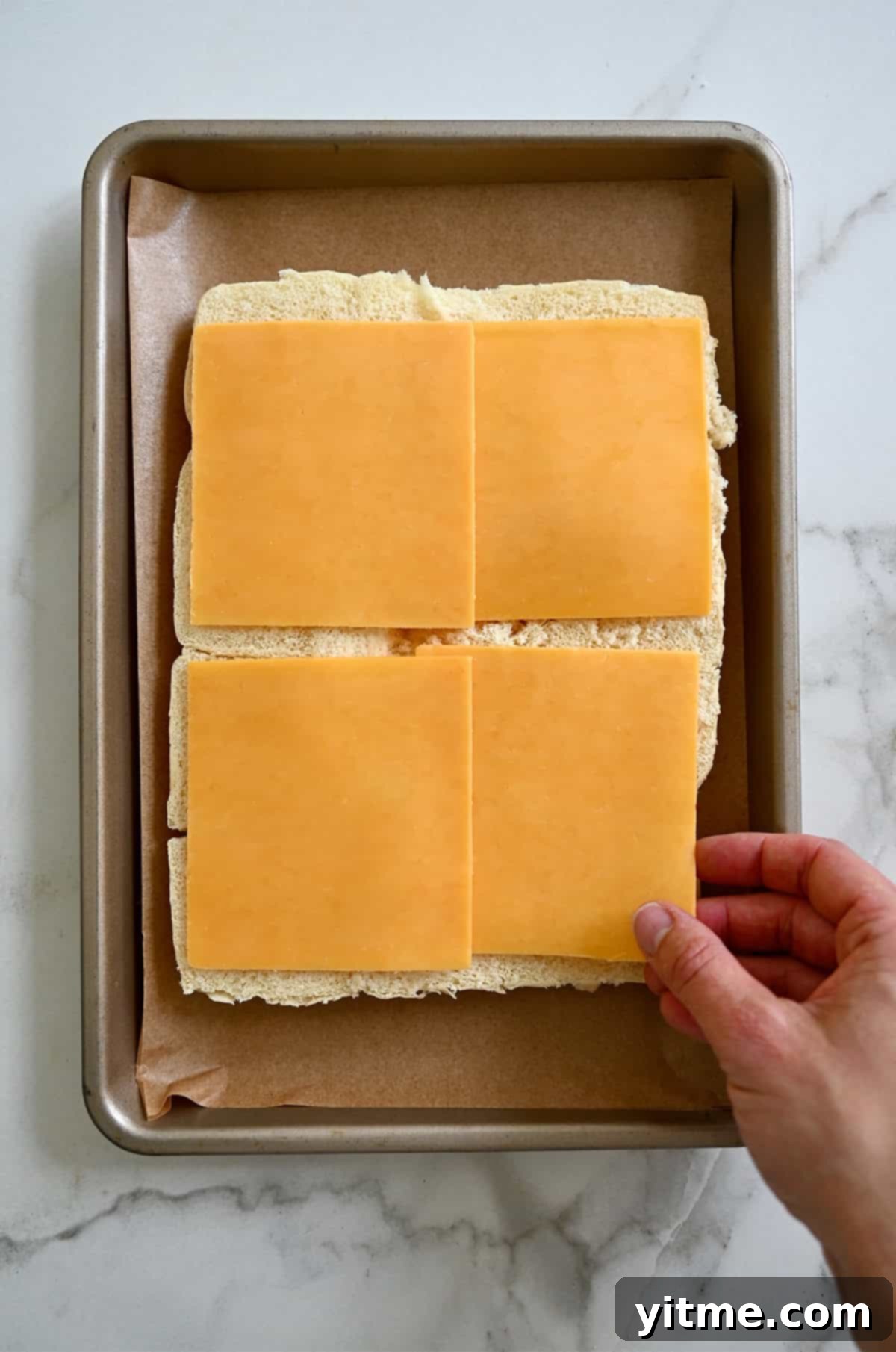Four slices of cheddar cheese atop halved Hawaiian rolls, forming the first cheese layer.