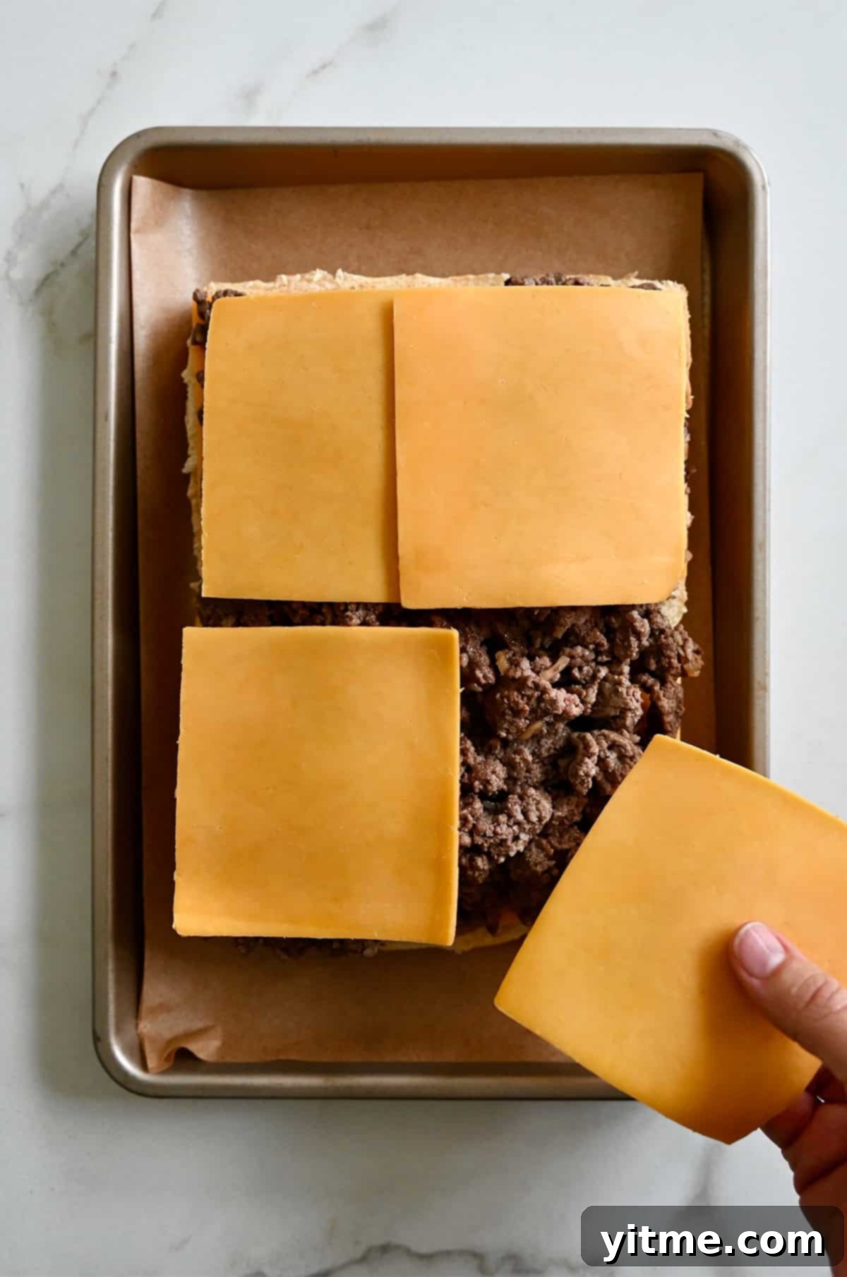 Buns topped with cooked burger meat being topped with the remaining slices of cheese.