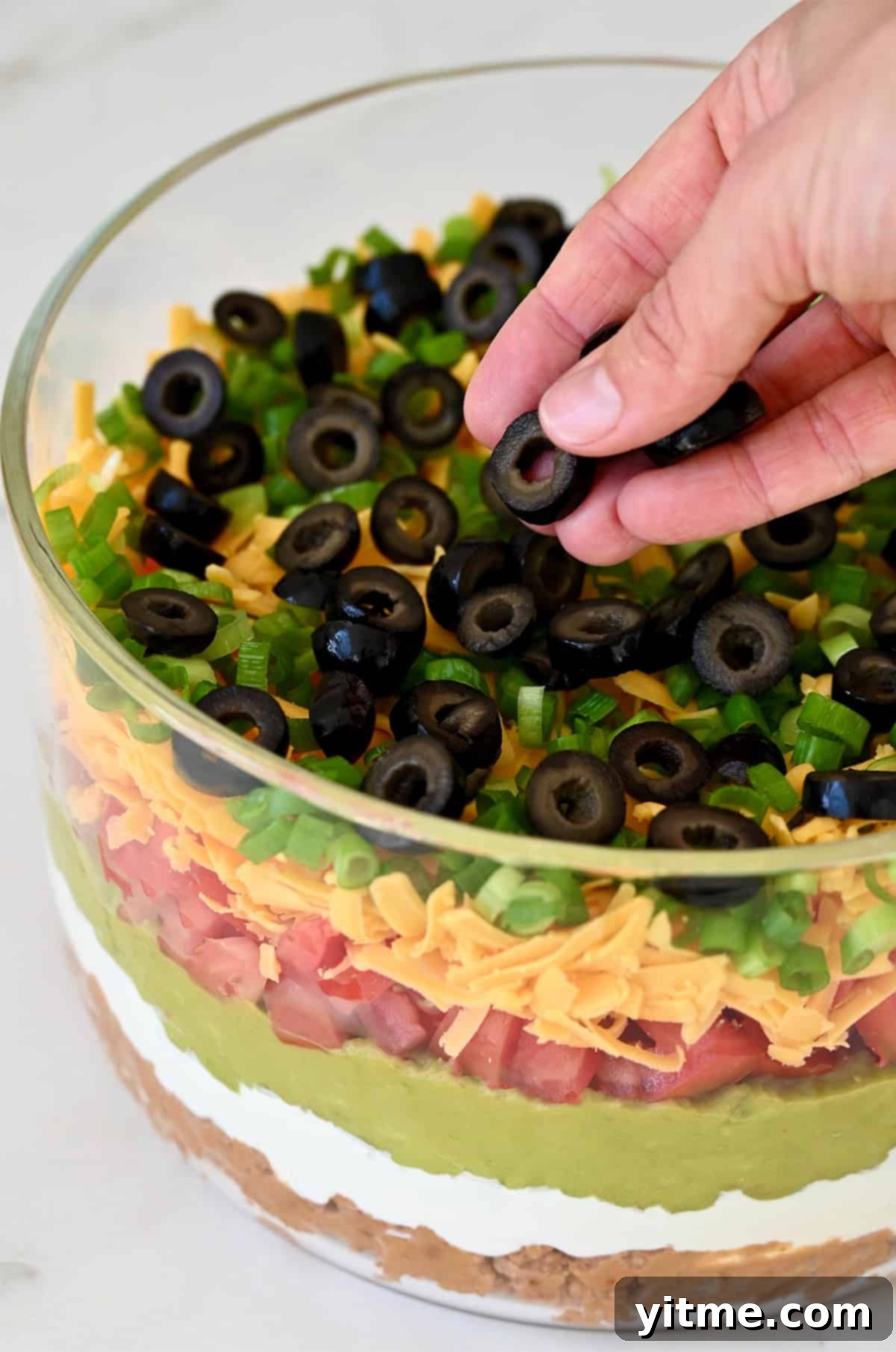 Adding sliced black olives as the final topping.