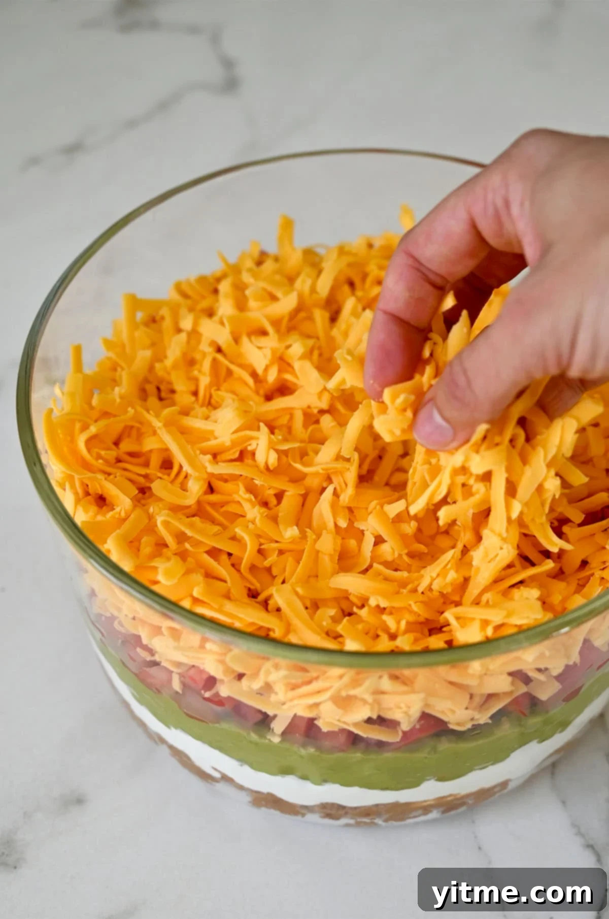 Spreading shredded cheese over the guacamole layer.