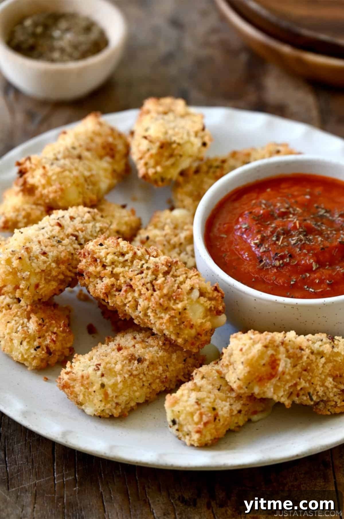 Homemade air fryer mozzarella sticks on a plate with a small bowl containing marinara sauce, ready to be enjoyed.