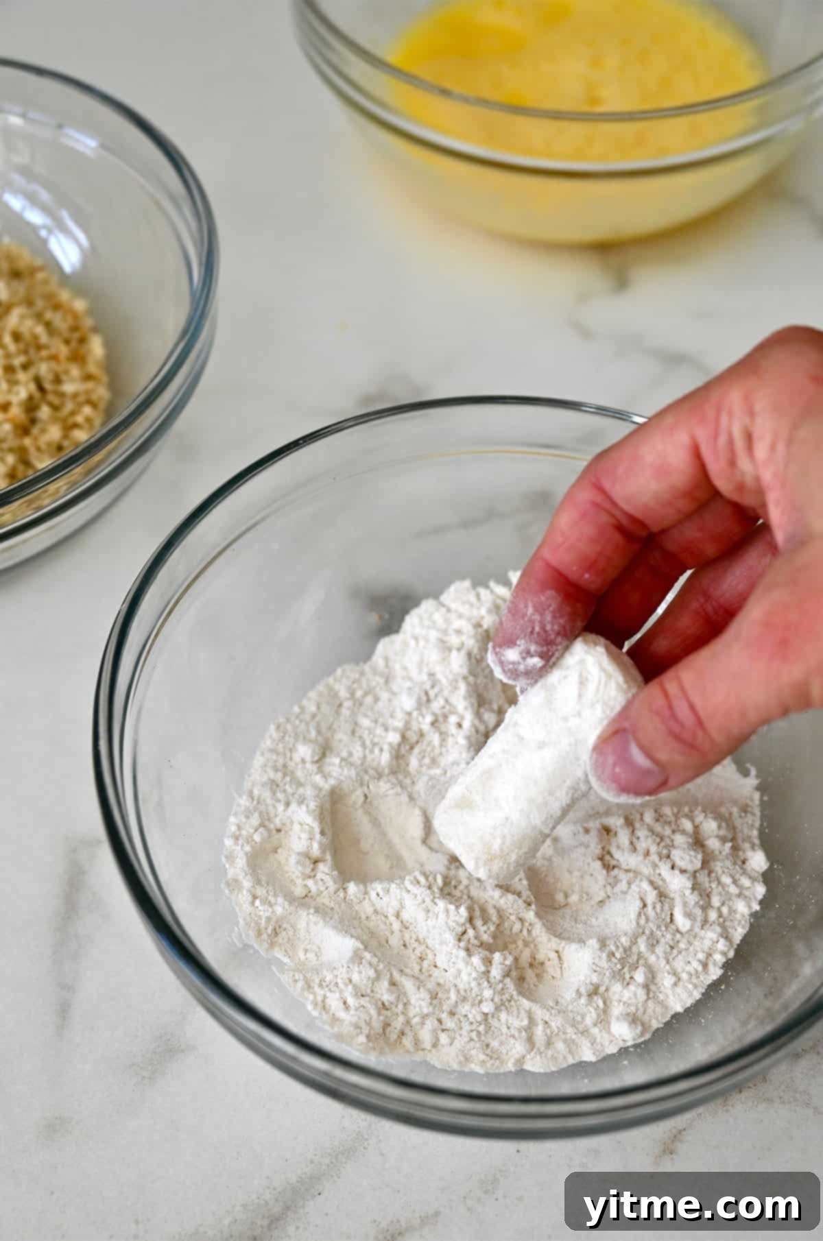 Dredging a mozzarella cheese stick in flour, ensuring even coverage.