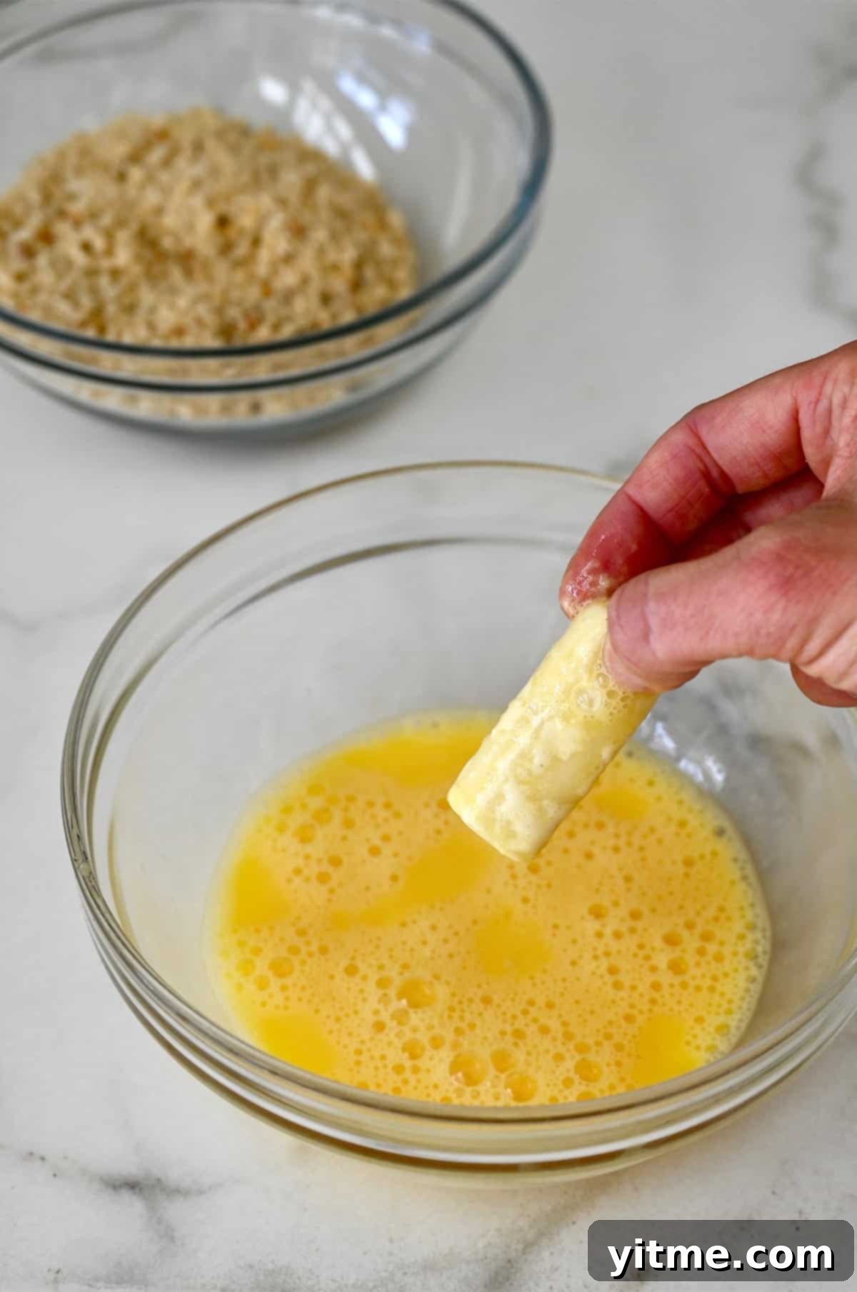 After flour, the mozzarella stick is coated with beaten egg, forming a sticky layer.