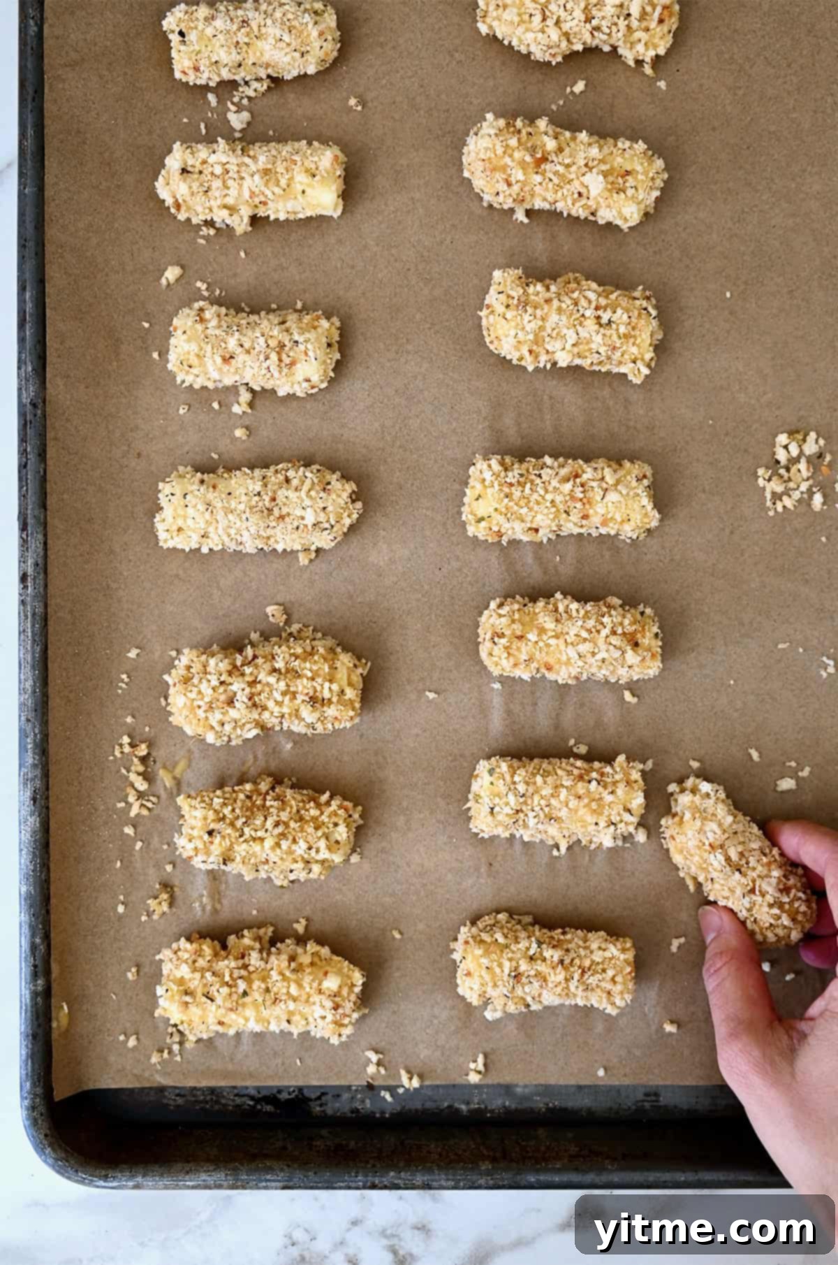 Frozen, breaded mozzarella sticks arranged in a single layer on a baking sheet lined with parchment paper.