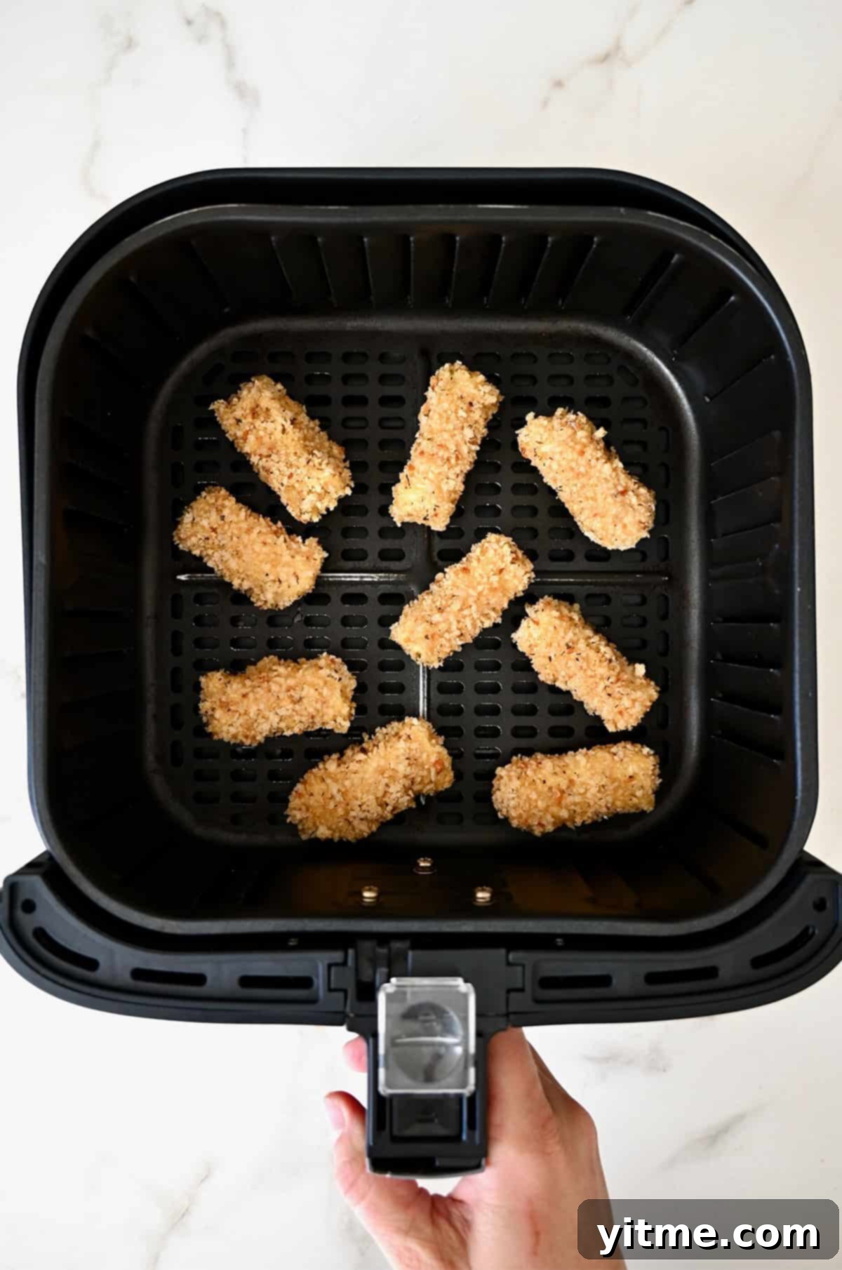 Homemade mozzarella sticks carefully placed in an air fryer basket, ready for cooking.