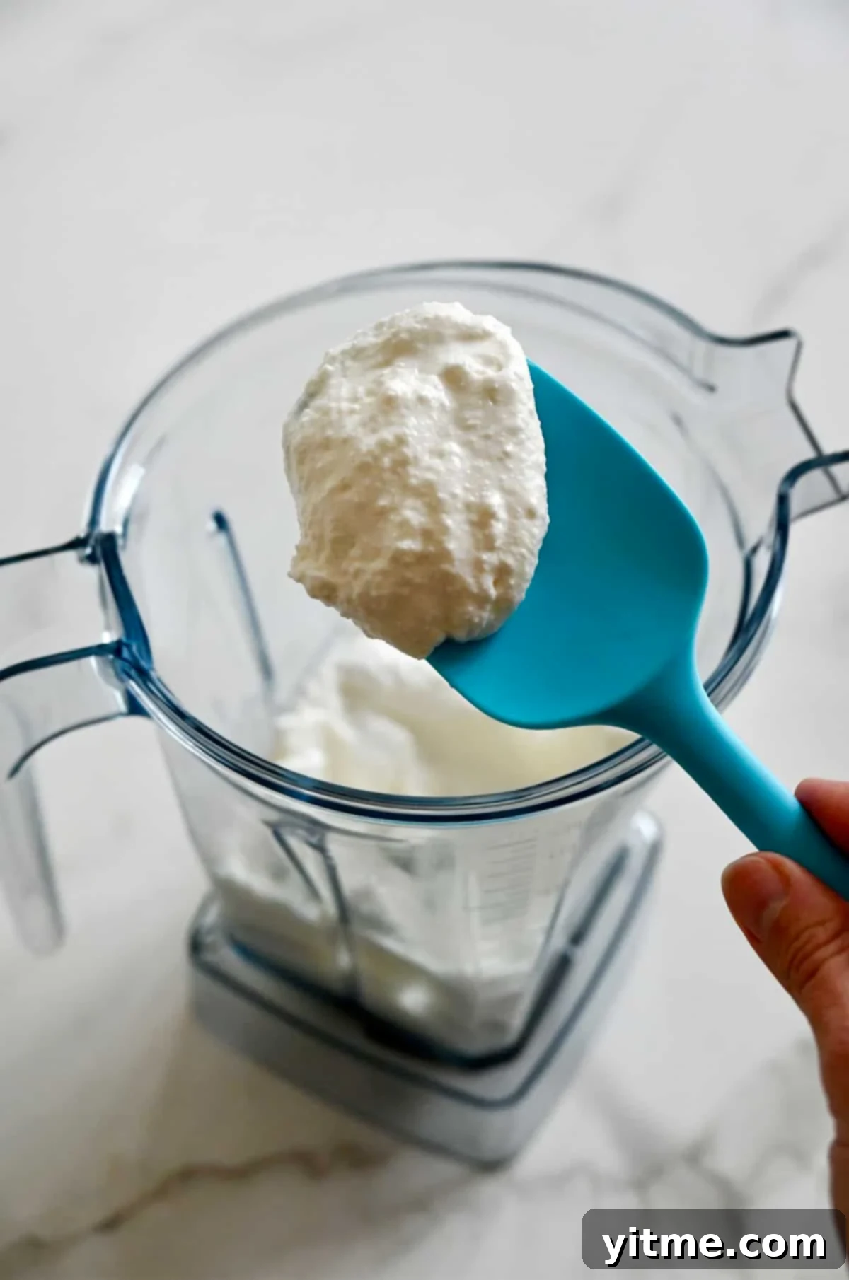 Blended cottage cheese covering a spatula above a high-powered blender.