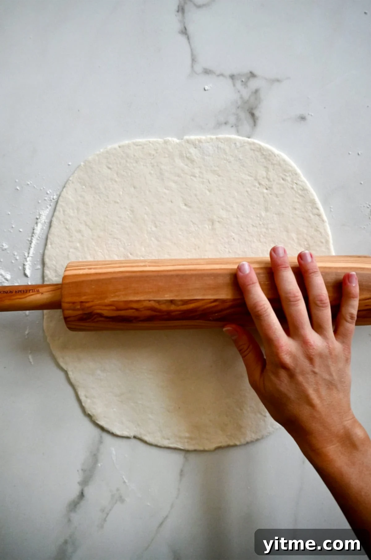 Rolling out pizza dough made with cottage cheese on a lightly floured surface.