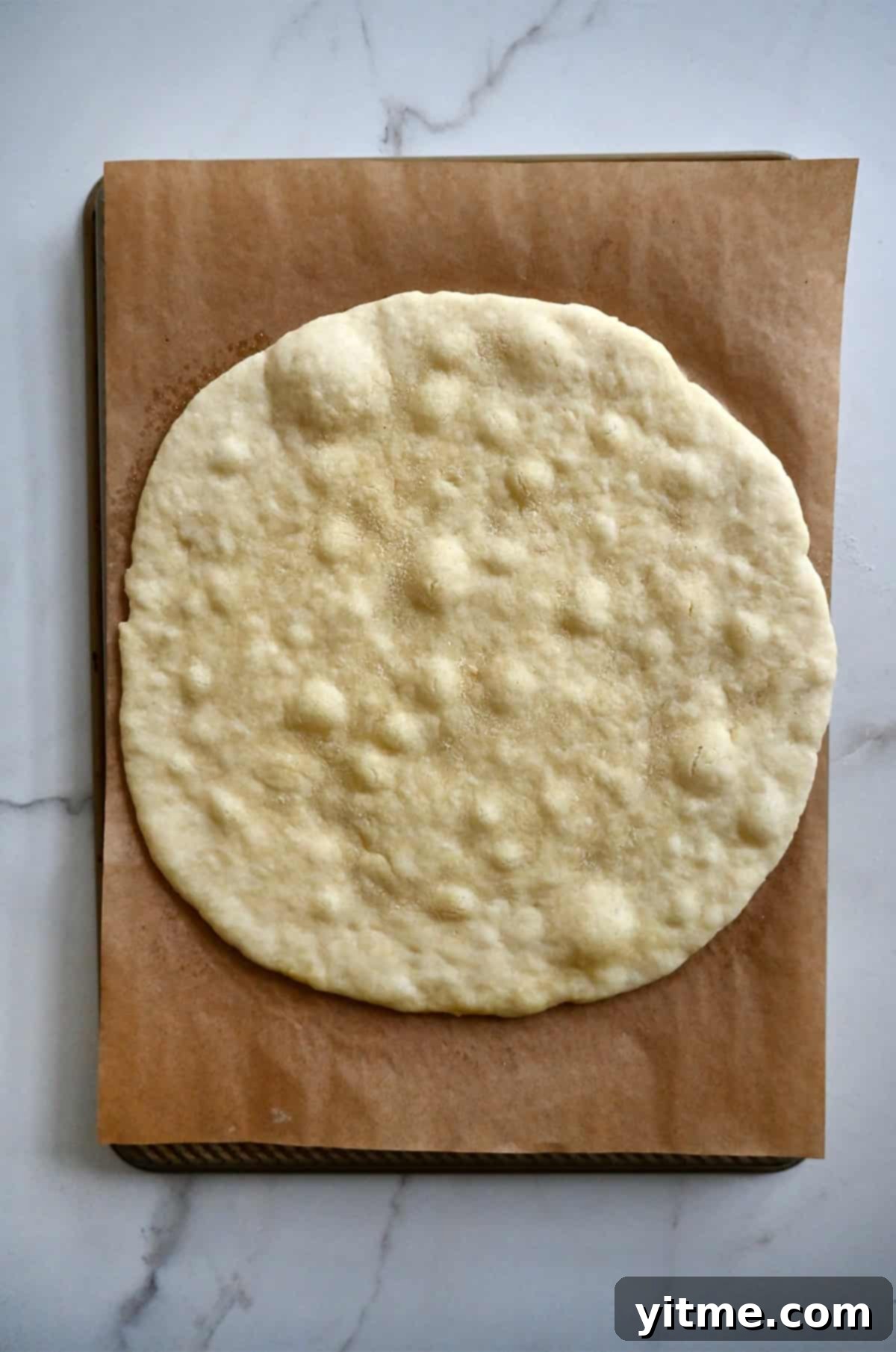 Par baked cottage cheese pizza crust on a parchment paper-lined baking sheet.