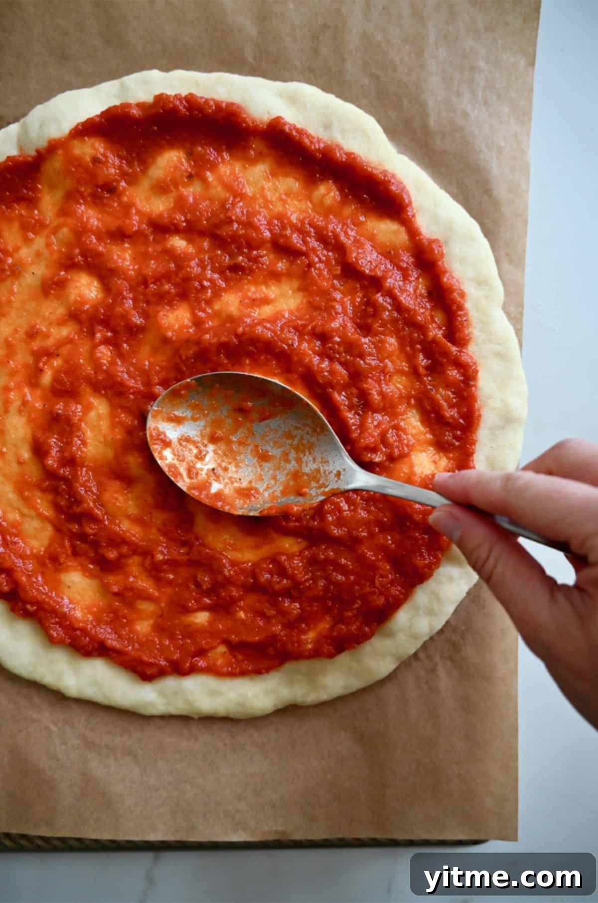 Using the back of a spoon to spread marinara sauce atop par baked pizza dough.