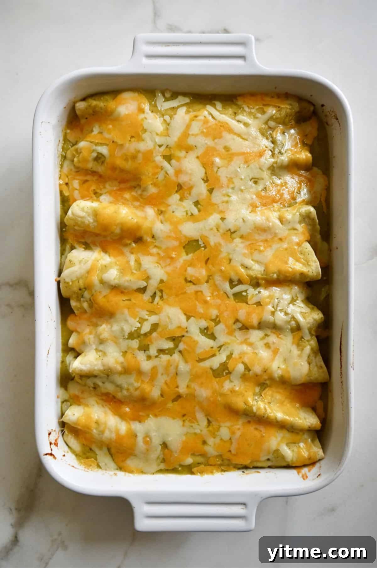 Melted cheese atop green Chile enchiladas in a white baking dish.