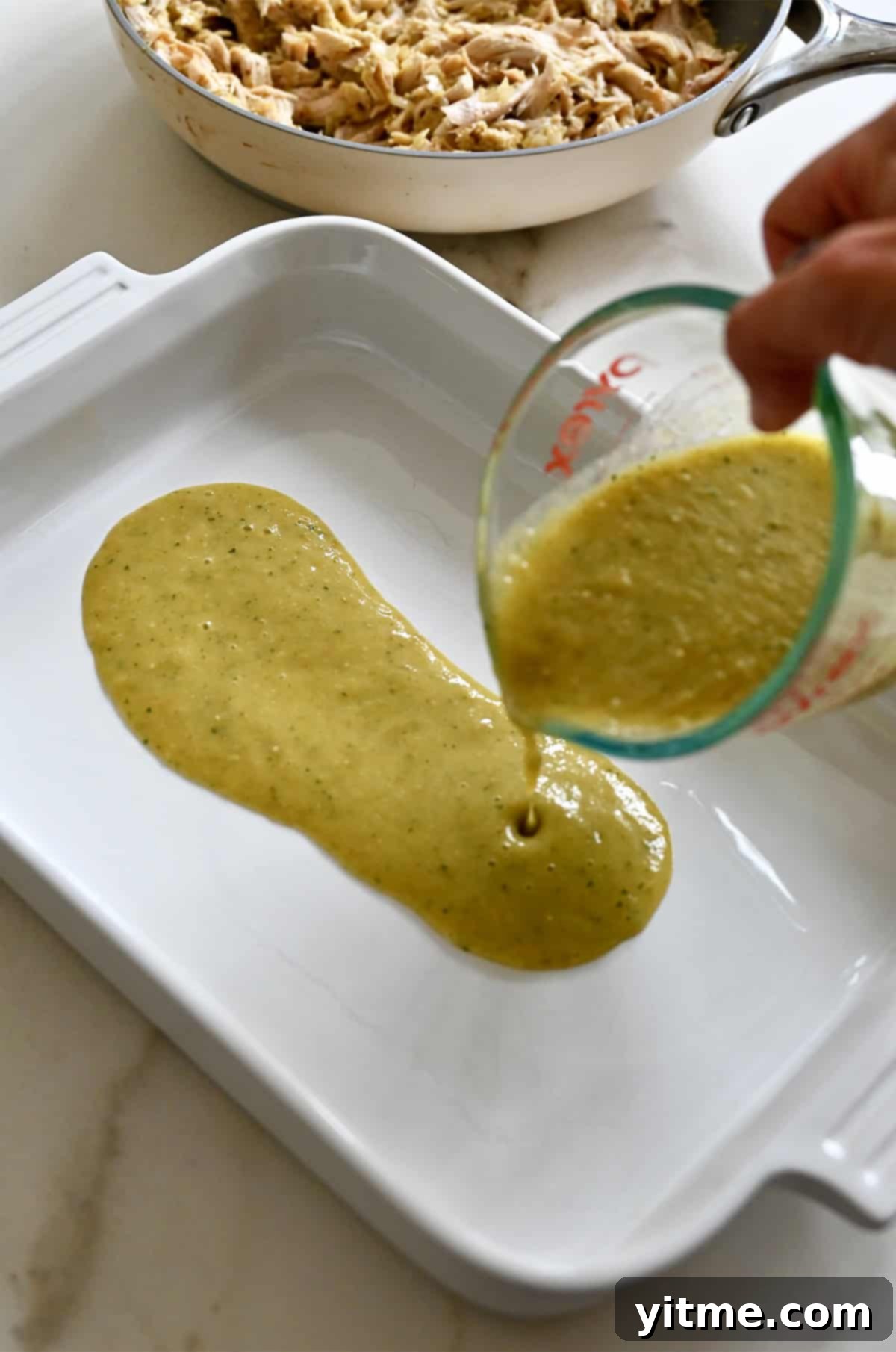 Pouring green salsa from a liquid measuring cup into a baking dish.