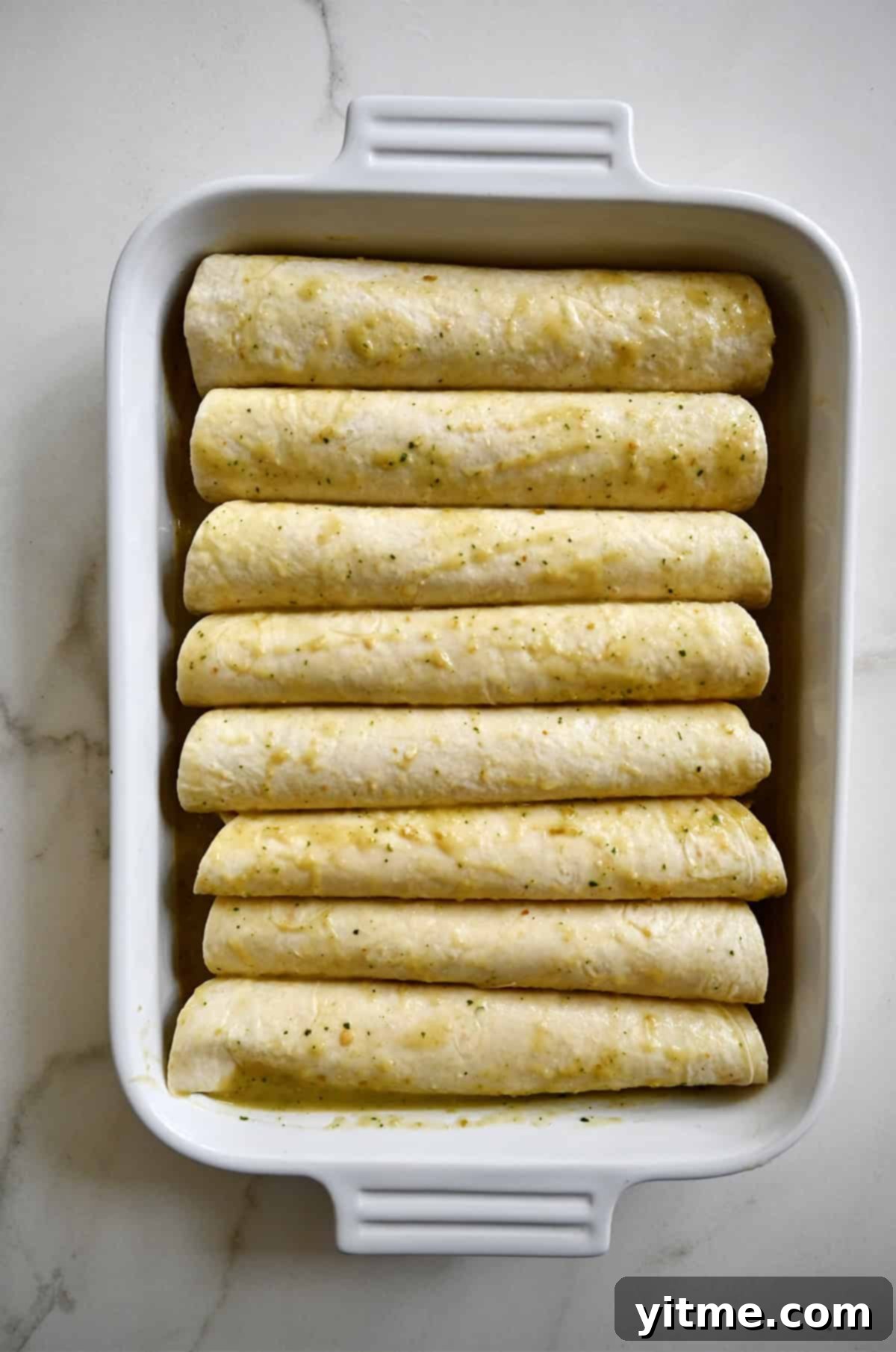 Rolled flour tortillas with chicken filling in a white baking dish.