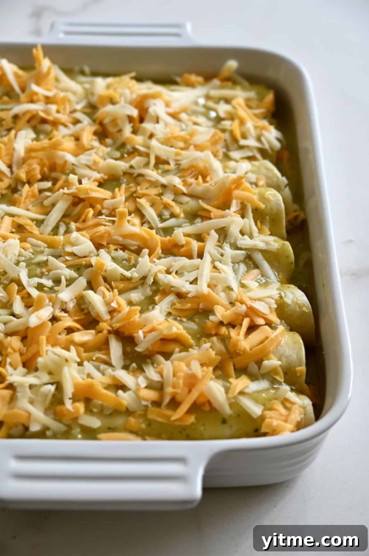 Unbaked enchiladas topped with shredded cheese.