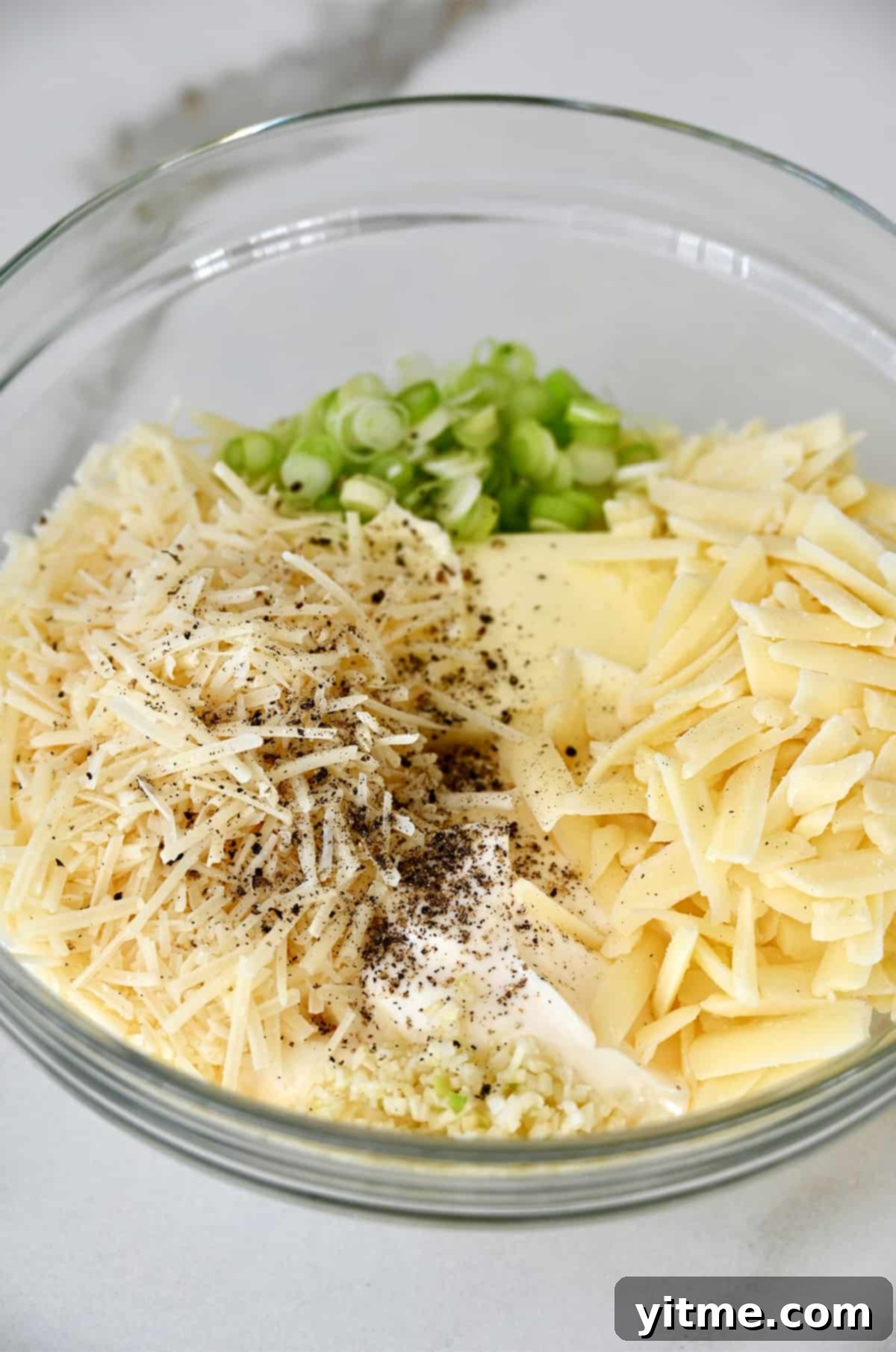 The Unexpected Twist: Cheesy Garlic Bread 4 A glass bowl containing butter, shredded Asiago and Monterey Jack cheese, sliced scallions, mayonnaise, salt, and pepper.