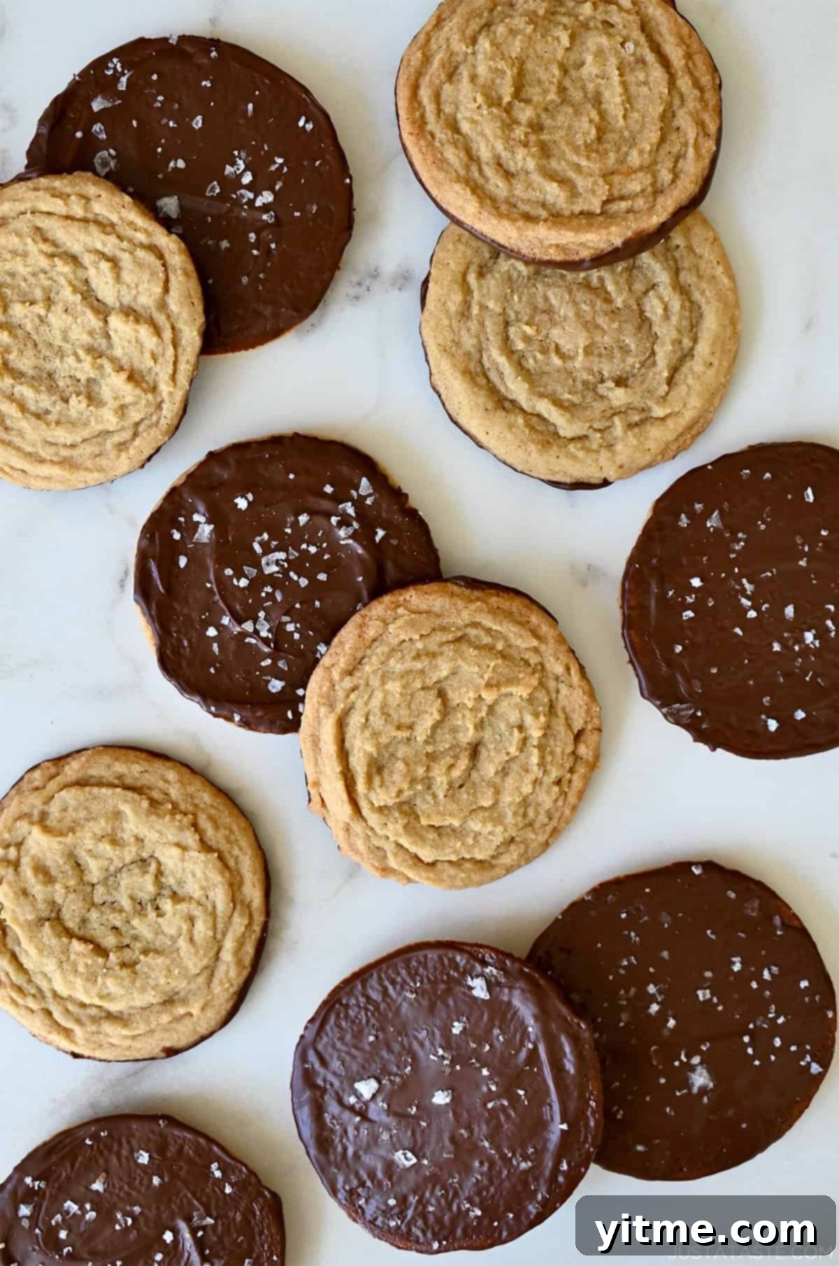 Vanilla Bean Dream Cookies 2 Chocolate chipless cookies, some dipped in chocolate and sprinkled with sea salt, on a marble countertop. A close-up showcasing the golden-brown perfection and the enticing salt crystals.