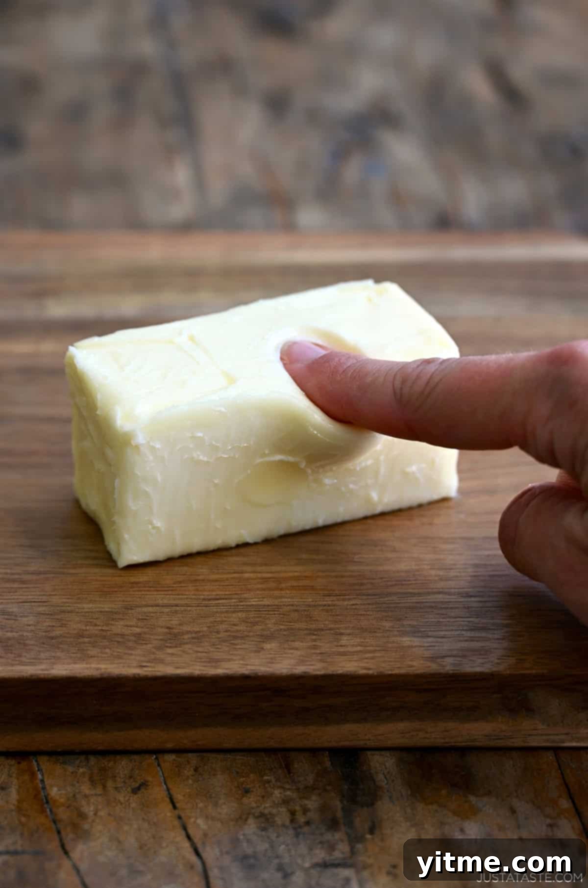 A finger pressing into softened butter to show ideal consistency.