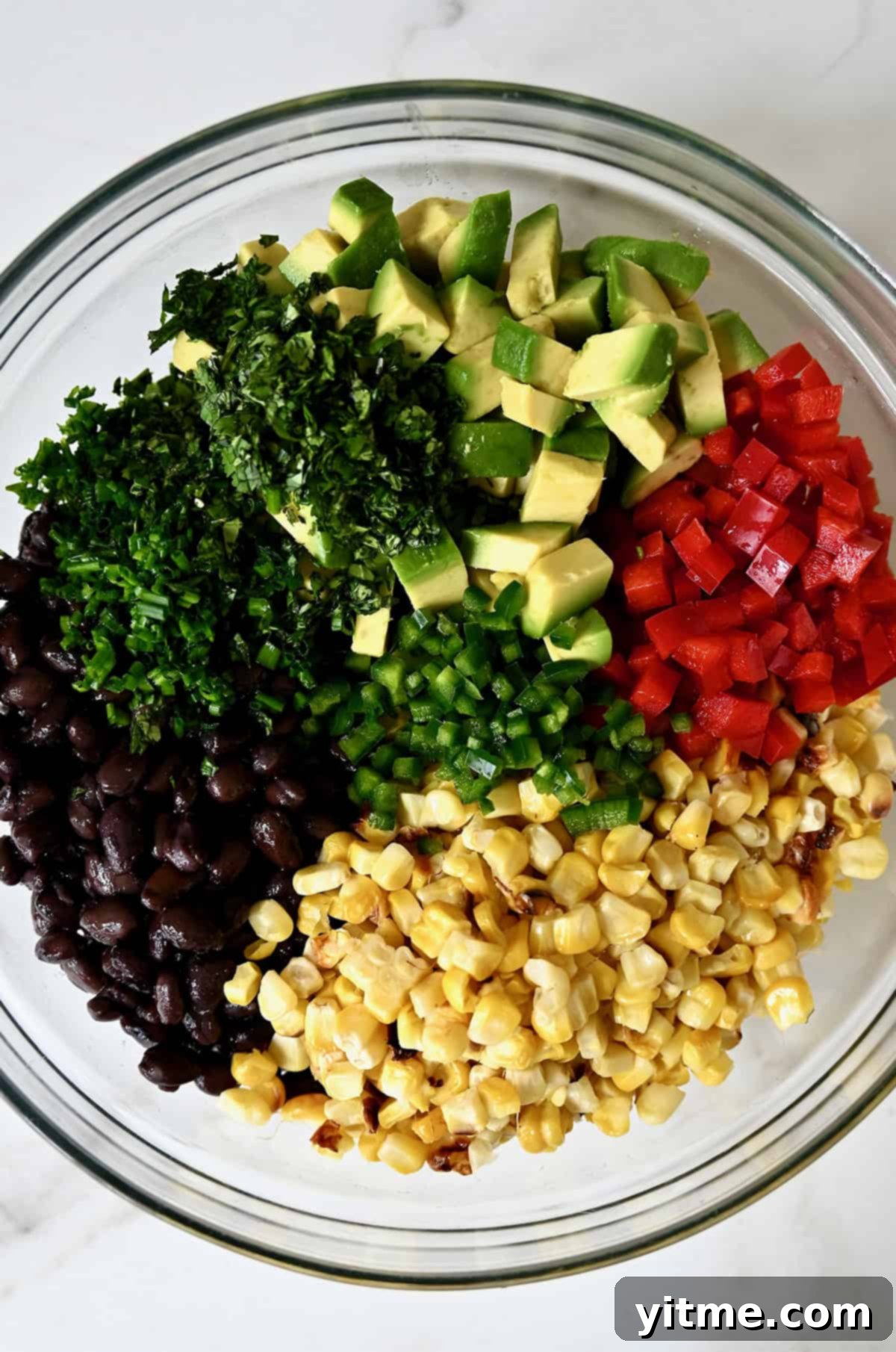 Black beans, cilantro, corn, avocado, bell pepper, chives, and jalapeño in a bowl.