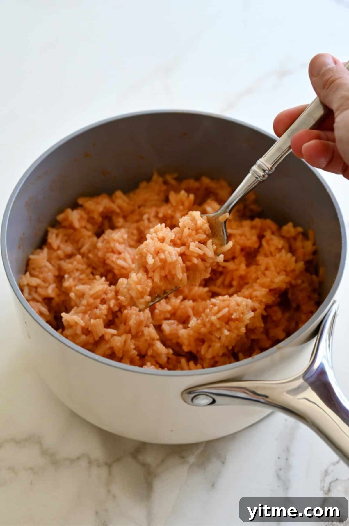 Fluffing Mexican rice with a fork in a saucepan, ready to be served as a taco bowl base.