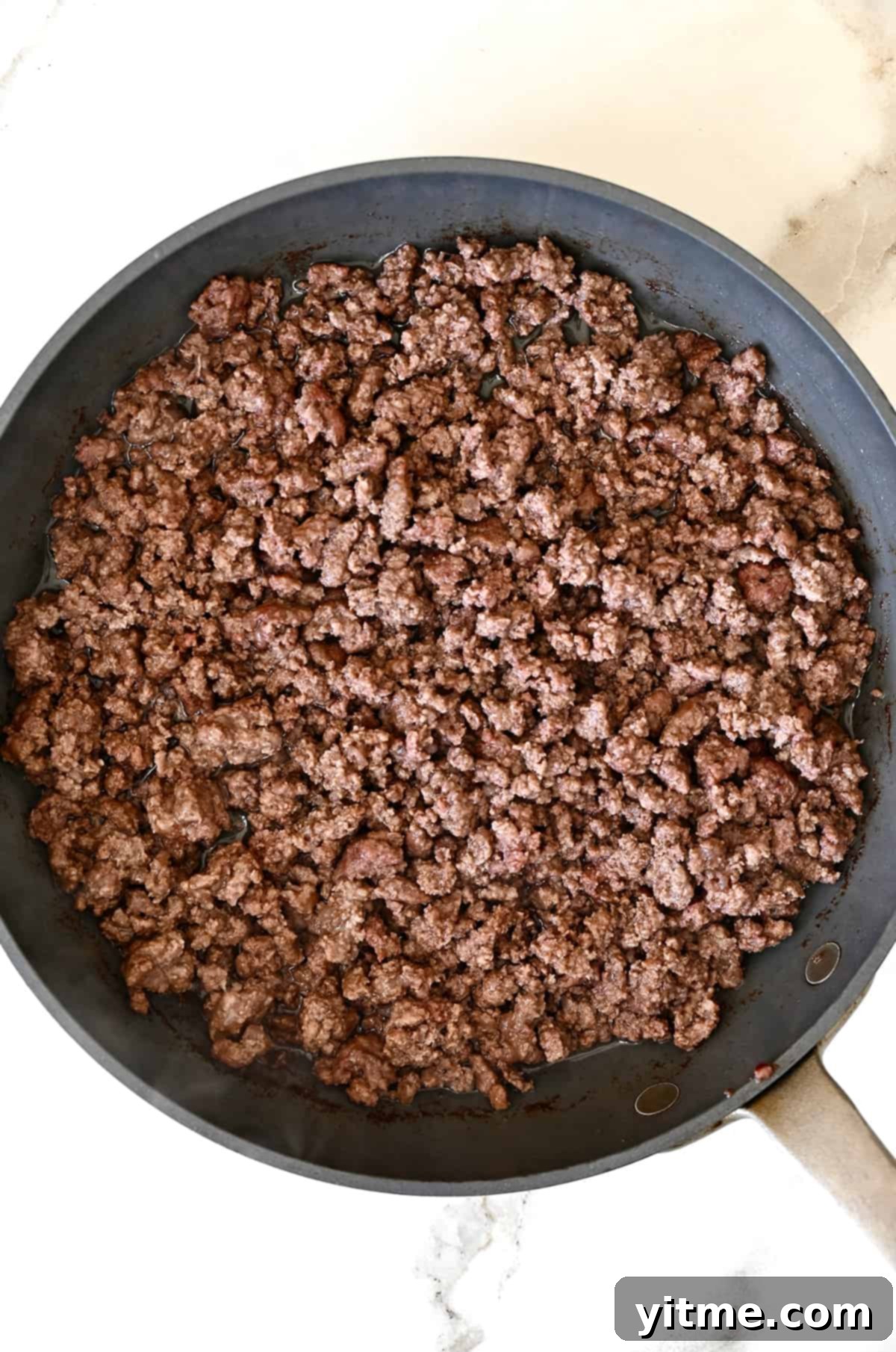 Sizzling browned ground beef in a large nonstick skillet, seasoned and ready for taco bowls.