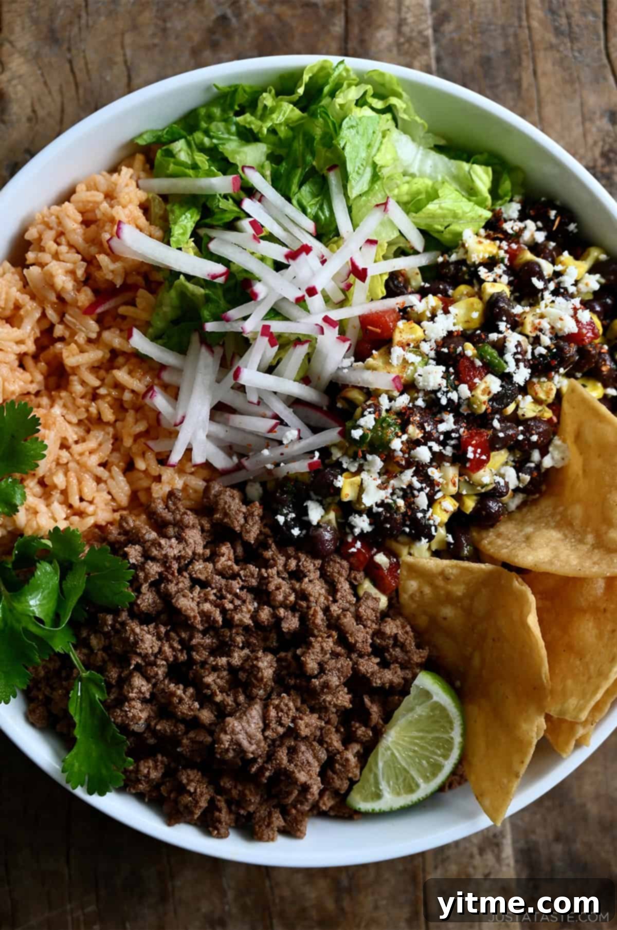 A satisfying ground beef taco bowl featuring shredded lettuce, fluffy Mexican rice, a colorful black bean and corn salsa, thinly sliced radishes, and crunchy tortilla chips, perfectly arranged for a wholesome meal.