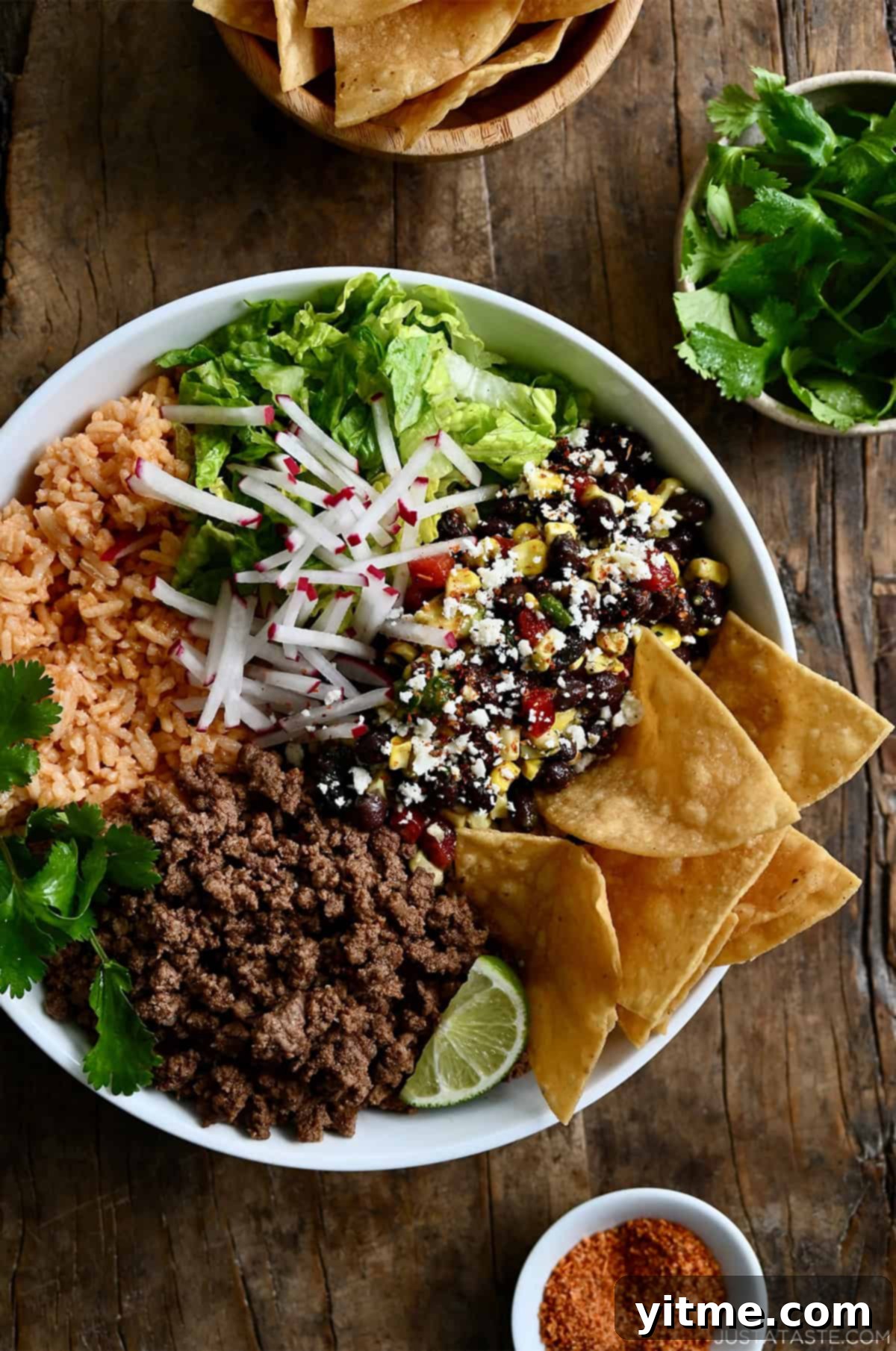 Taco meat in a bowl with Mexican rice, shredded lettuce, black bean and corn salad, sliced radishes, cilantro, a wedge of lime, and tortilla chips.