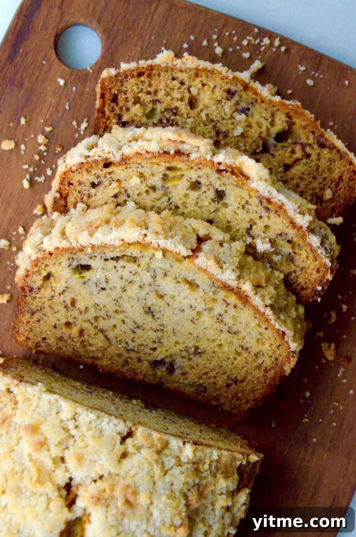 A loaf of banana bread with streusel topping on a wooden cutting board with a couple of slices cut off of it.