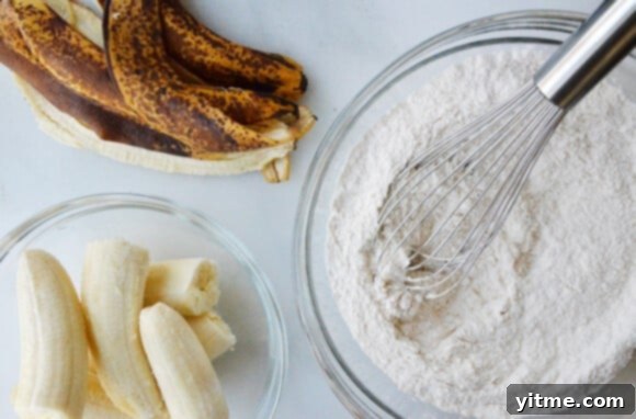 Dry ingredients in a large glass mixing bowl and peeled bananas in another glass mixing bowl.