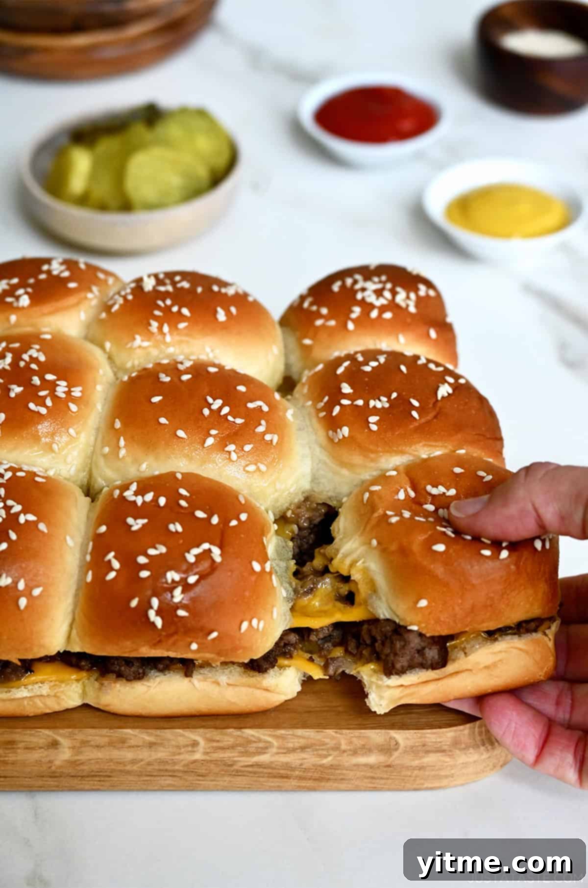 Pull-apart cheeseburger sliders on Hawaiian rolls with a bowl filled with pickles nearby. These sliders are sweet, savory, and gooey with cheese, making them a crowd-pleasing appetizer or meal.