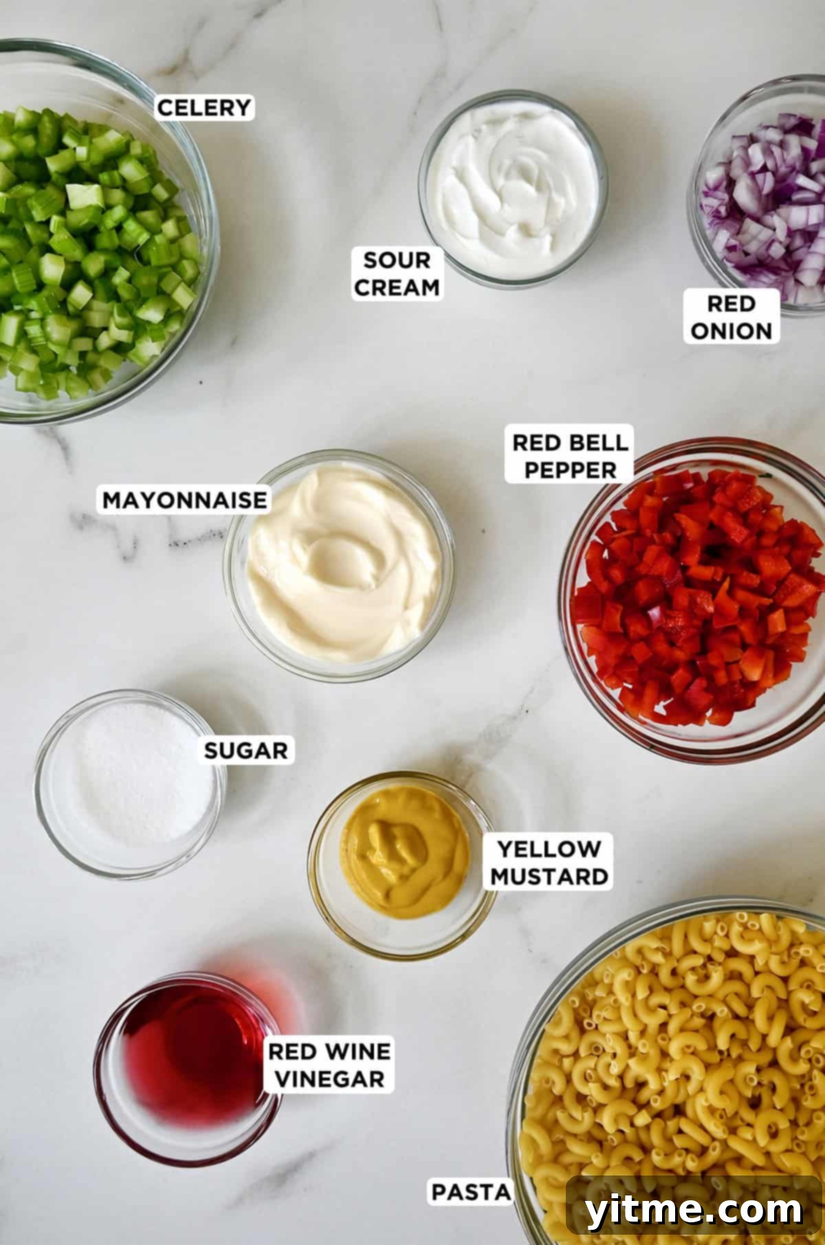 Ingredients to make macaroni salad in various sizes of glass bowls.