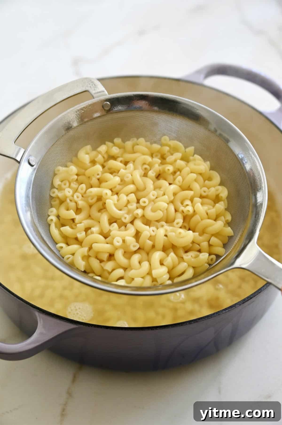 Al dente elbow pasta in a mesh strainer over a pot of salted water.