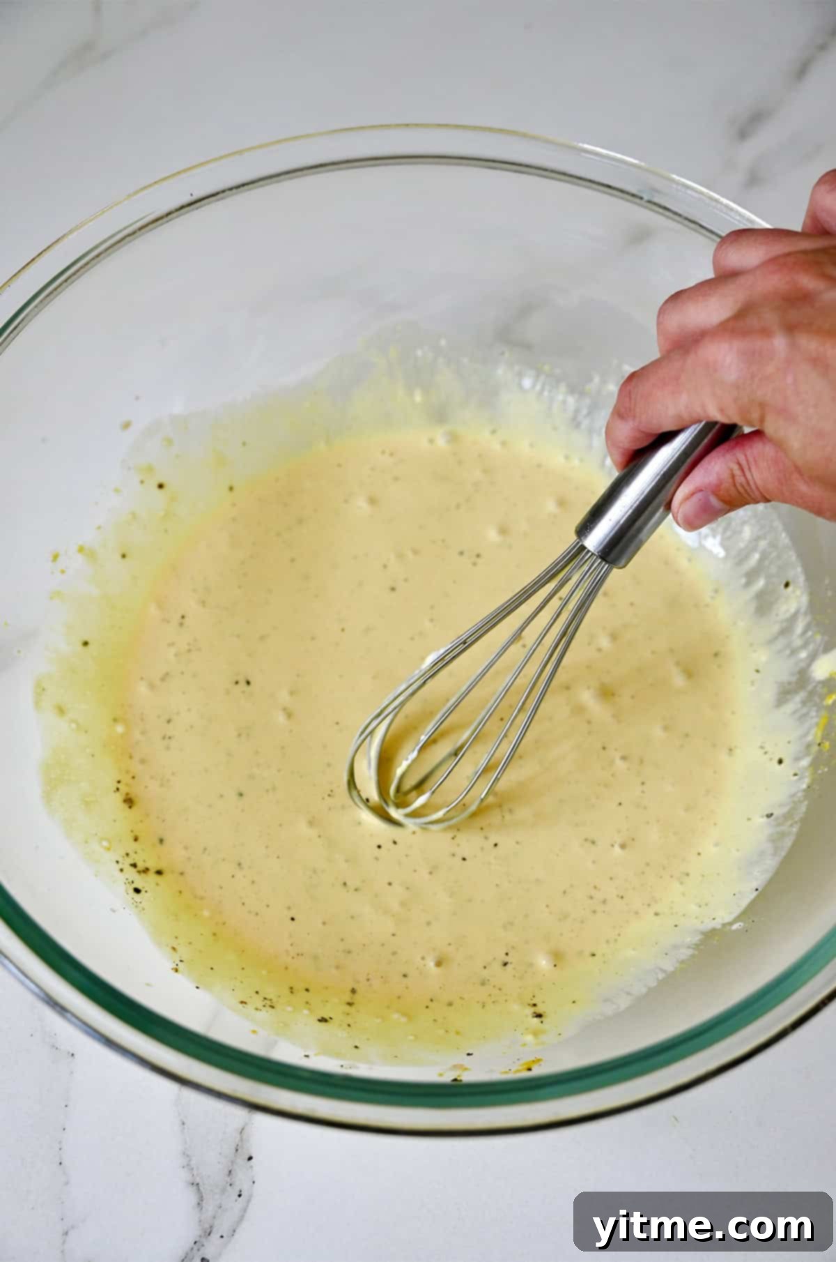 Creamy mayo-based pasta salad dressing is being whisked in a bowl.