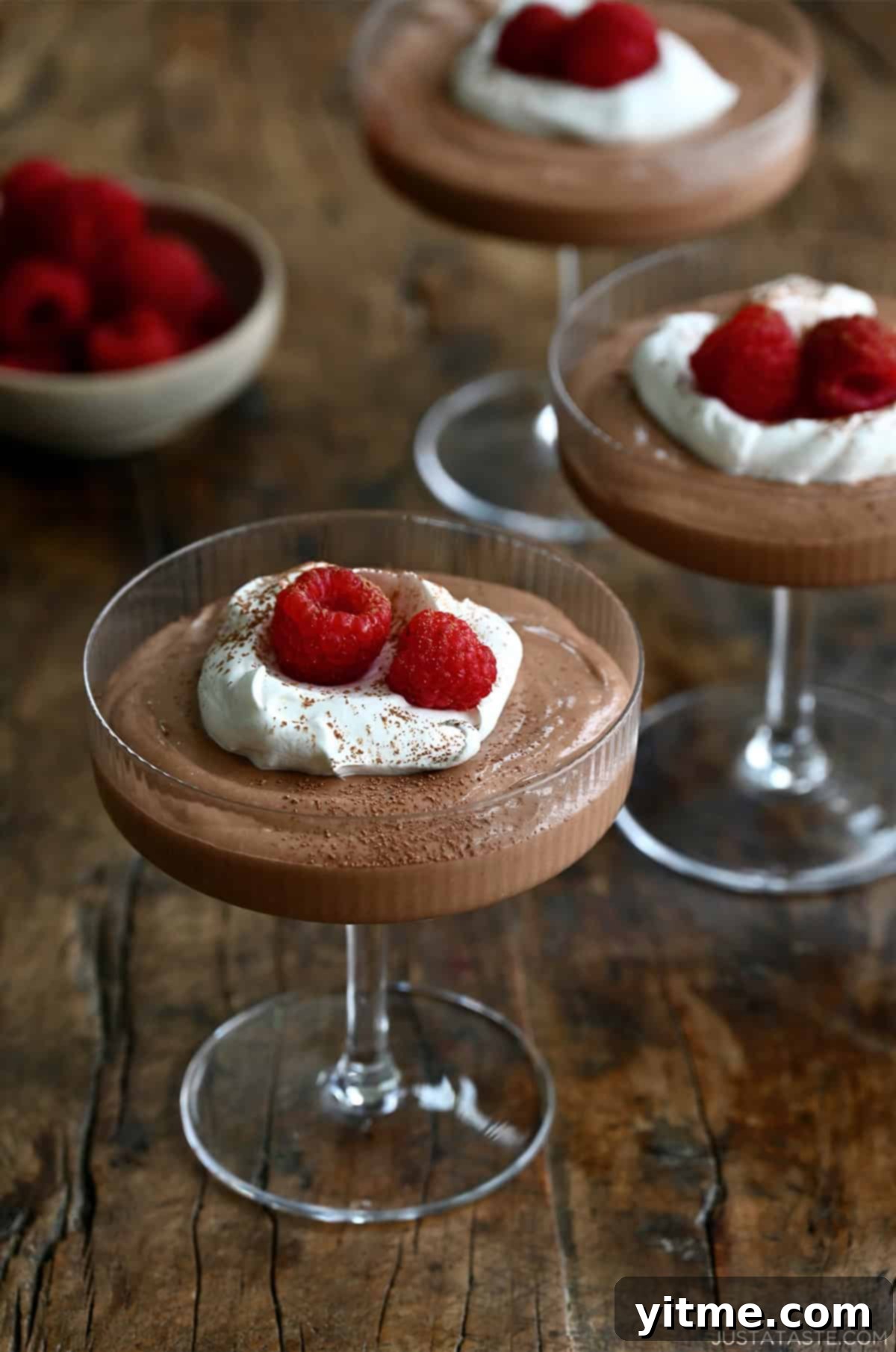 Clear glasses containing Cottage Cheese Chocolate Mousse topped with whipped cream and raspberries - A healthy and delicious alternative to traditional chocolate mousse.
