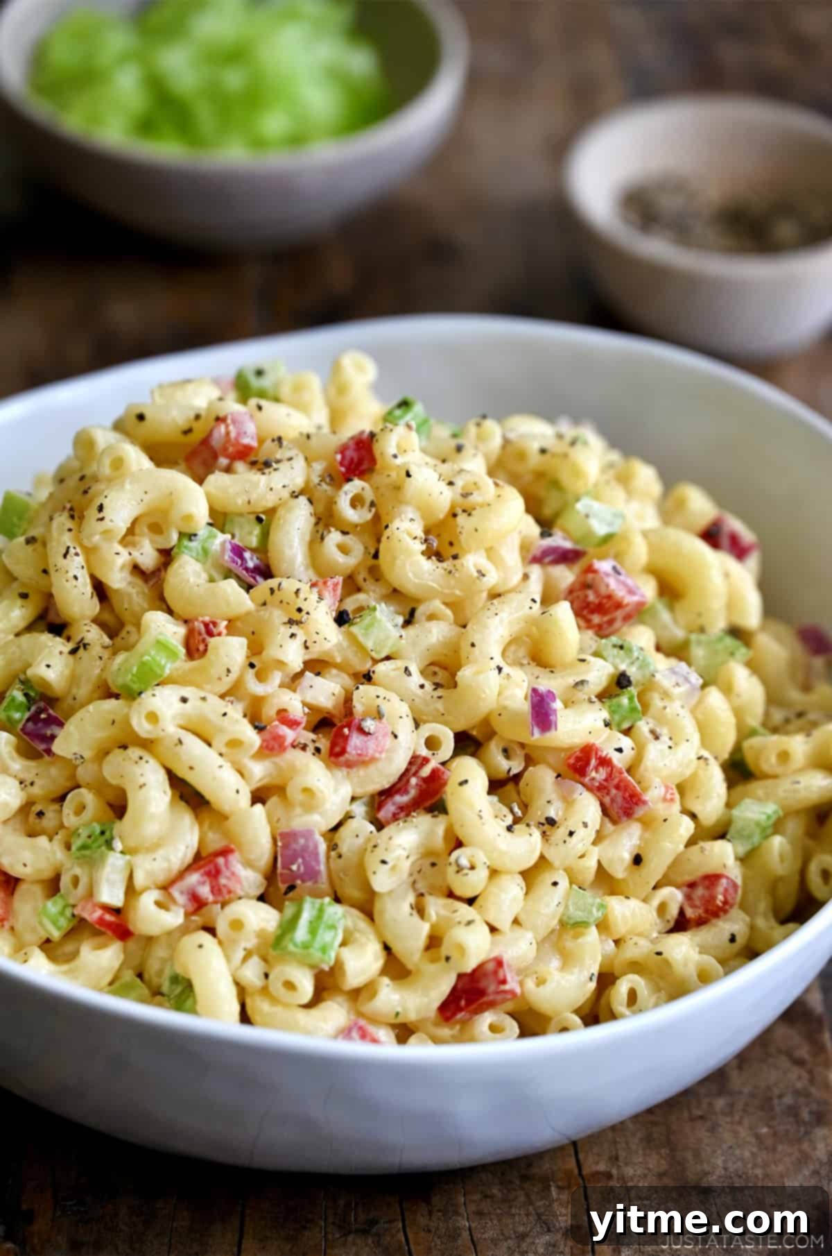 A serving bowl containing macaroni salad with diced red onion, diced celery and diced red bell pepper, all tossed in a creamy homemade dressing - A summer staple for picnics and potlucks.