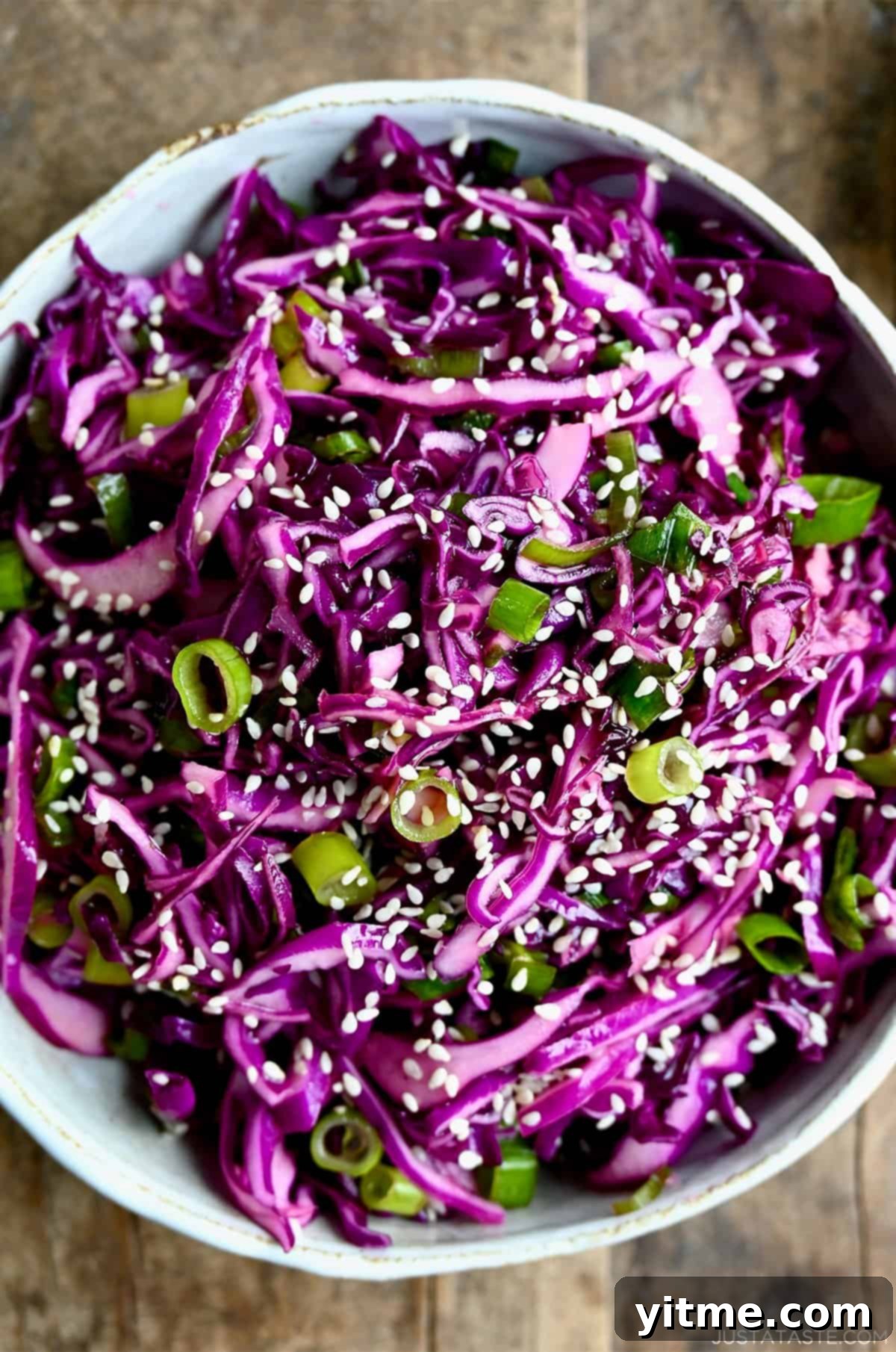 Large white serving bowl filled with vibrant Asian slaw, featuring shredded purple cabbage, fresh lime wedges, and a hint of sesame oil.