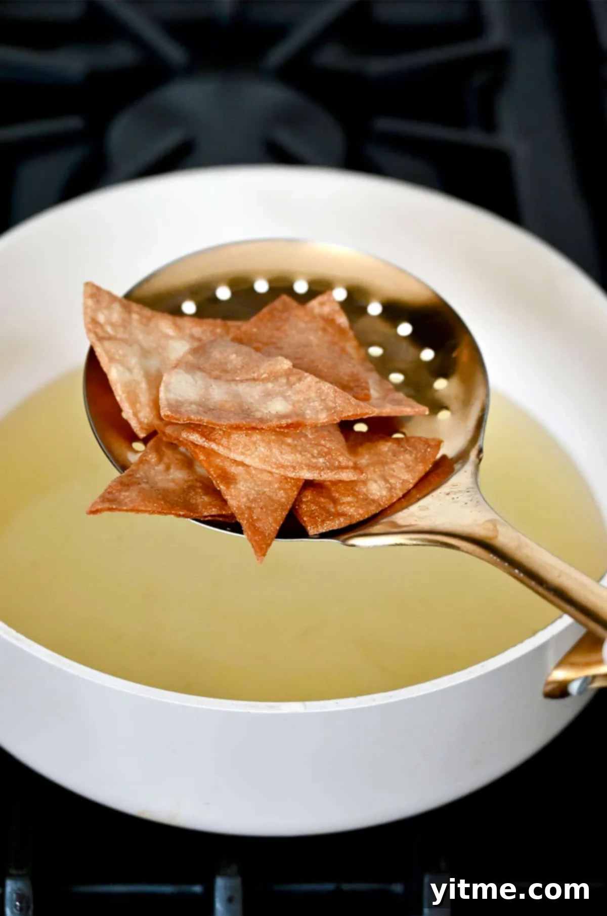 Crispy Homemade Tortilla Chips: Two Ways to Deliciousness 6 Fried tortilla chips on a slotted spoon above a large pot with hot oil.