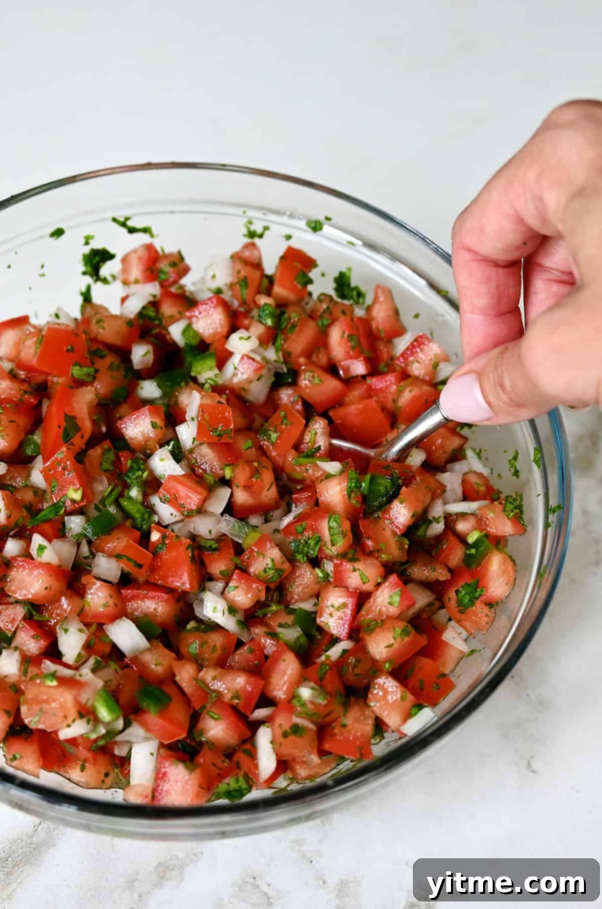 Mixing all the ingredients for pico de gallo in a bowl with a spoon.