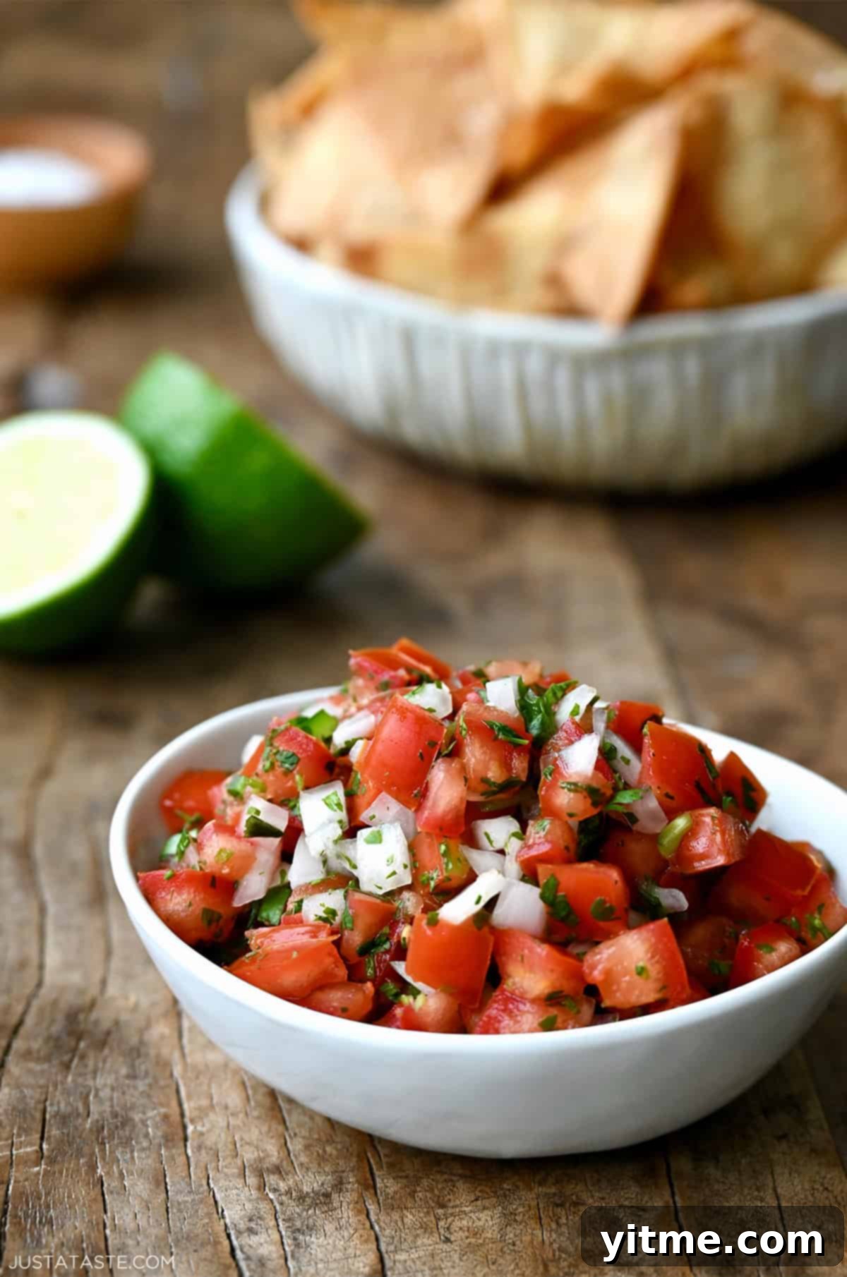Fresh homemade pico de gallo in a small bowl near another bowl filled with tortilla chips.