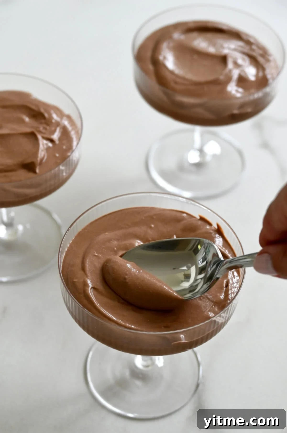 A spoon spreading chocolate mousse into coupe glasses.