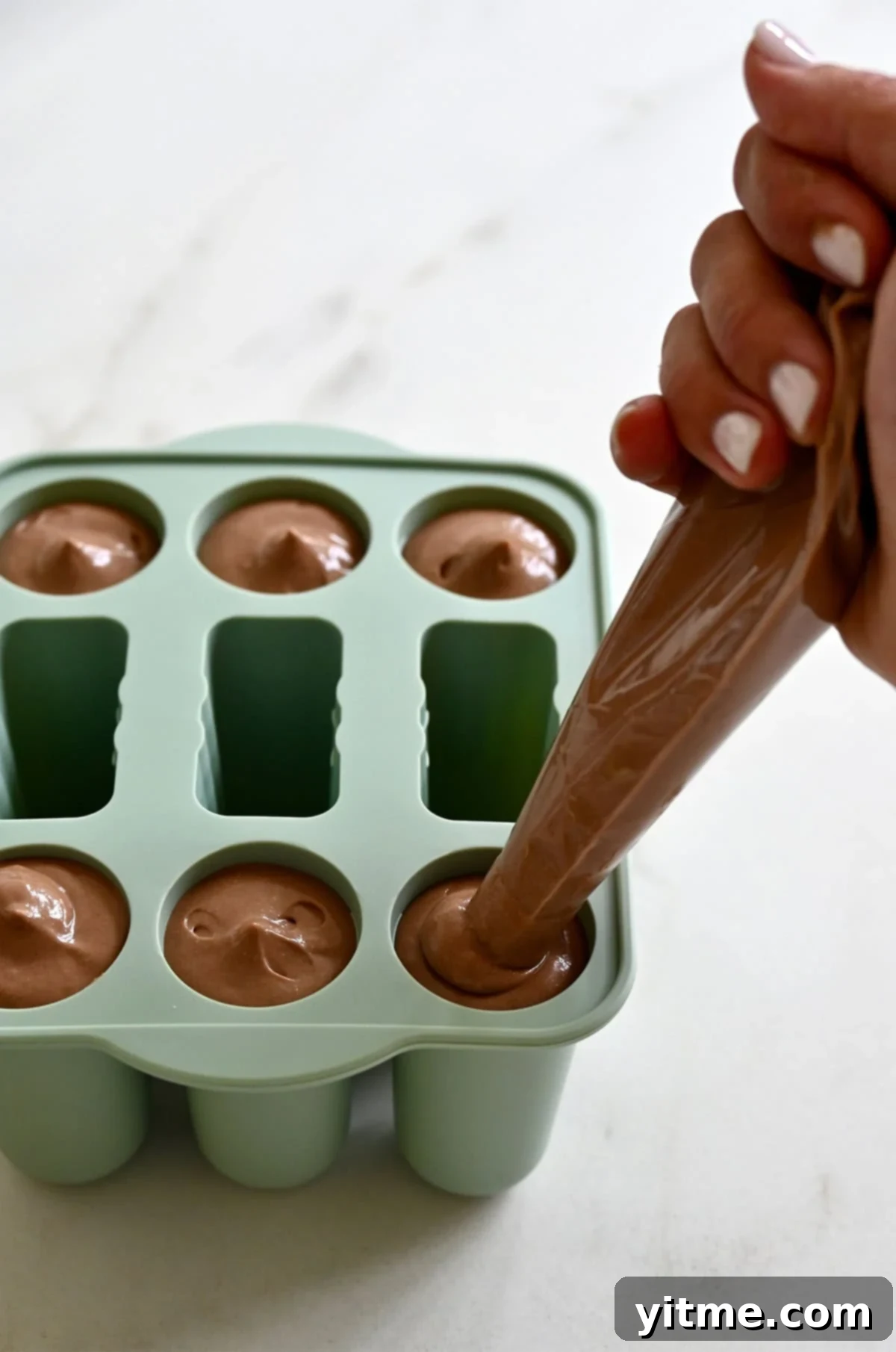 Piping cottage cheese chocolate mousse from a plastic bag into a silicone popsicle mold.