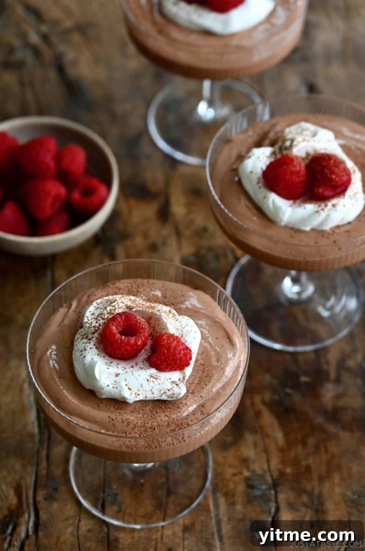 Three coupe glasses filled with chocolate mousse and sitting on a wooden surface