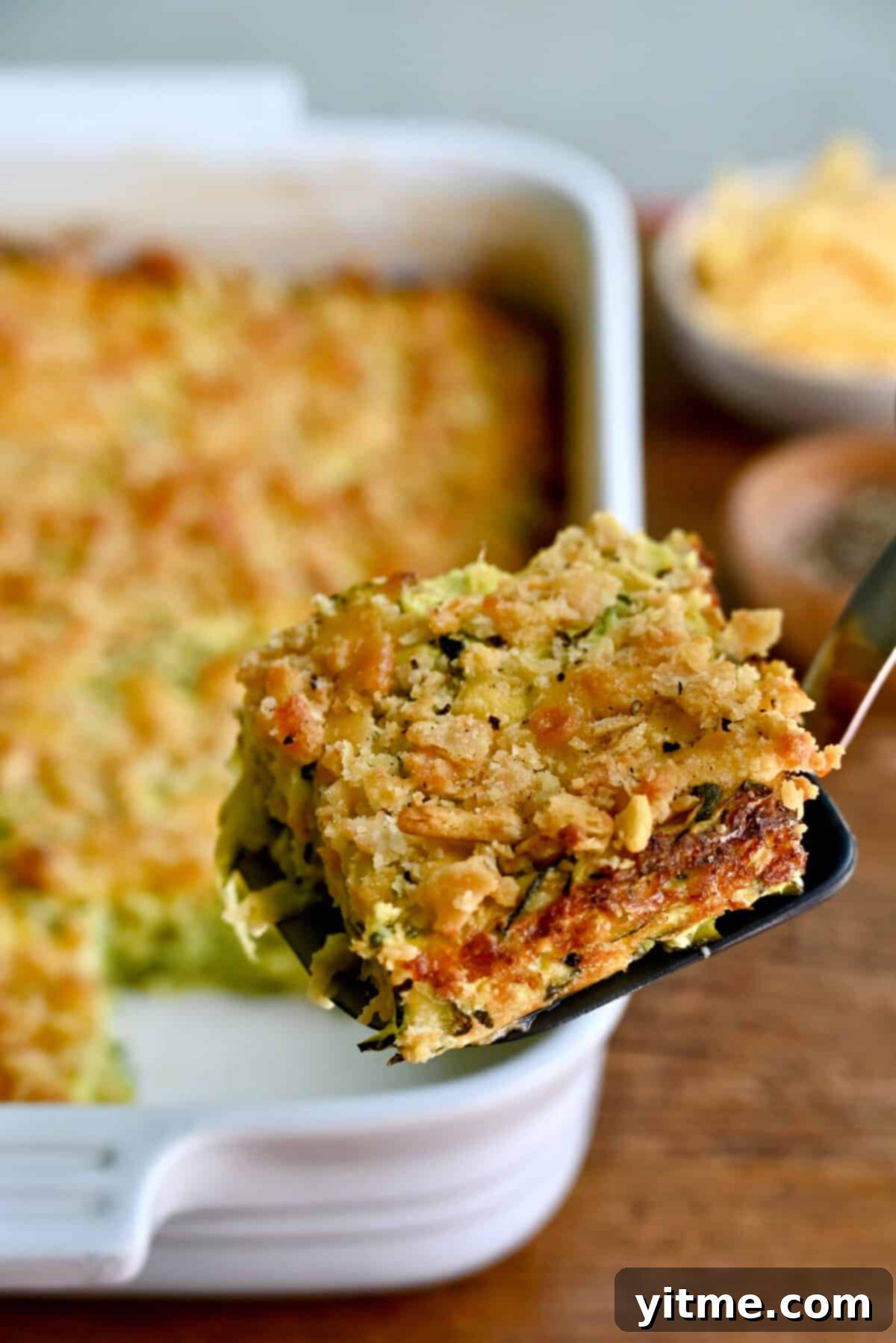 A slice of cheesy zucchini casserole on a spatula, showcasing its creamy interior and golden-brown crust.