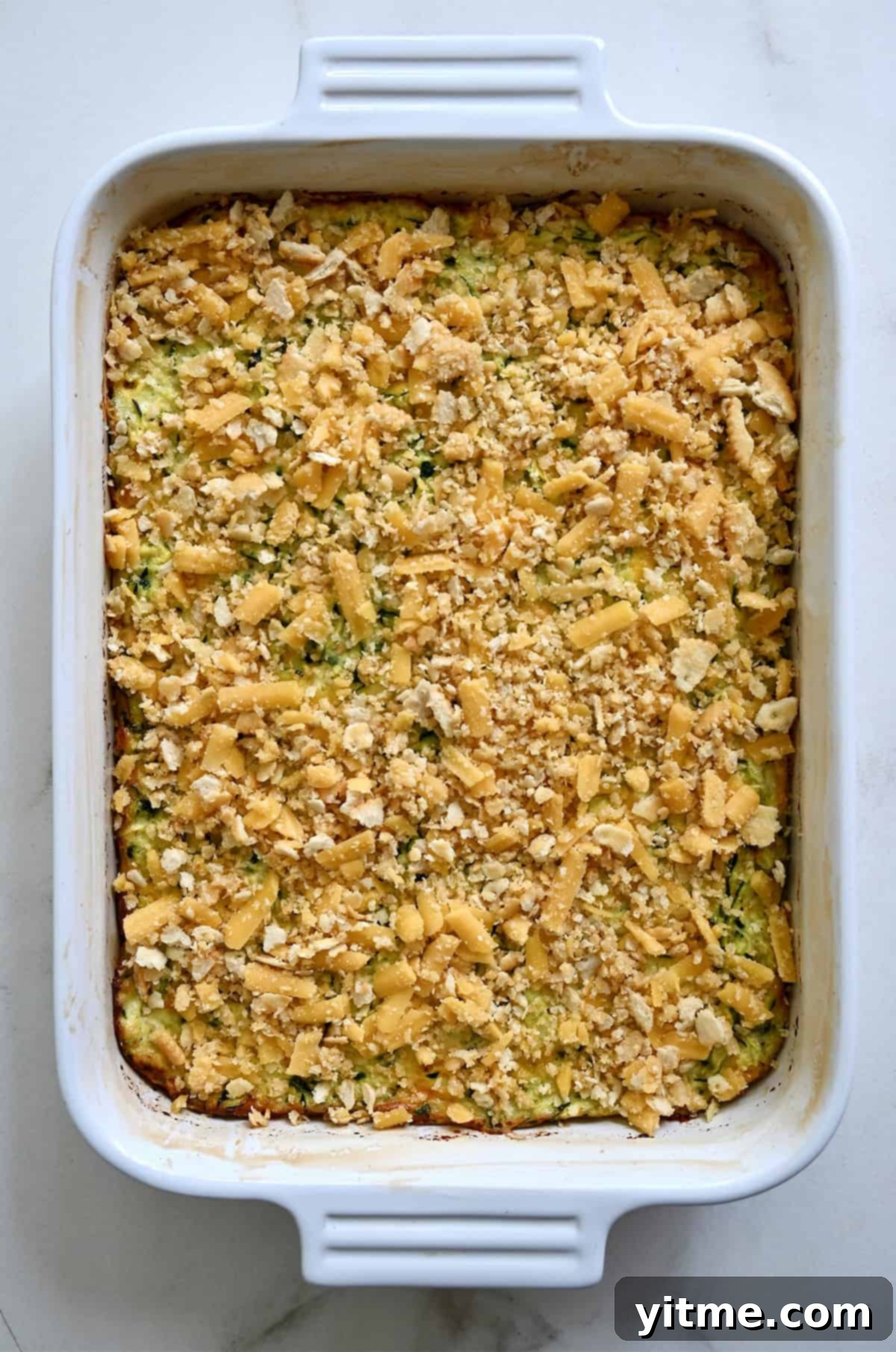 Untoasted cheese and cracker topping atop a casserole in a 9x13 baking dish.