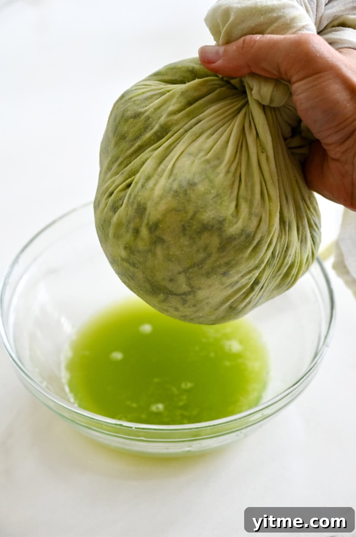 Squeezing excess moisture from shredded zucchini in a cheese cloth over a bowl.