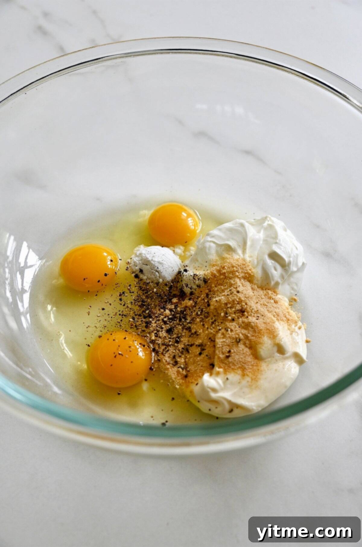 Sour cream, mayonnaise, garlic powder, onion powder, baking powder, and eggs in a glass bowl.