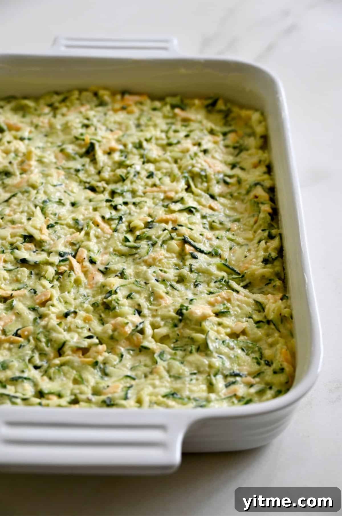Unbaked squash casserole in a white baking dish.