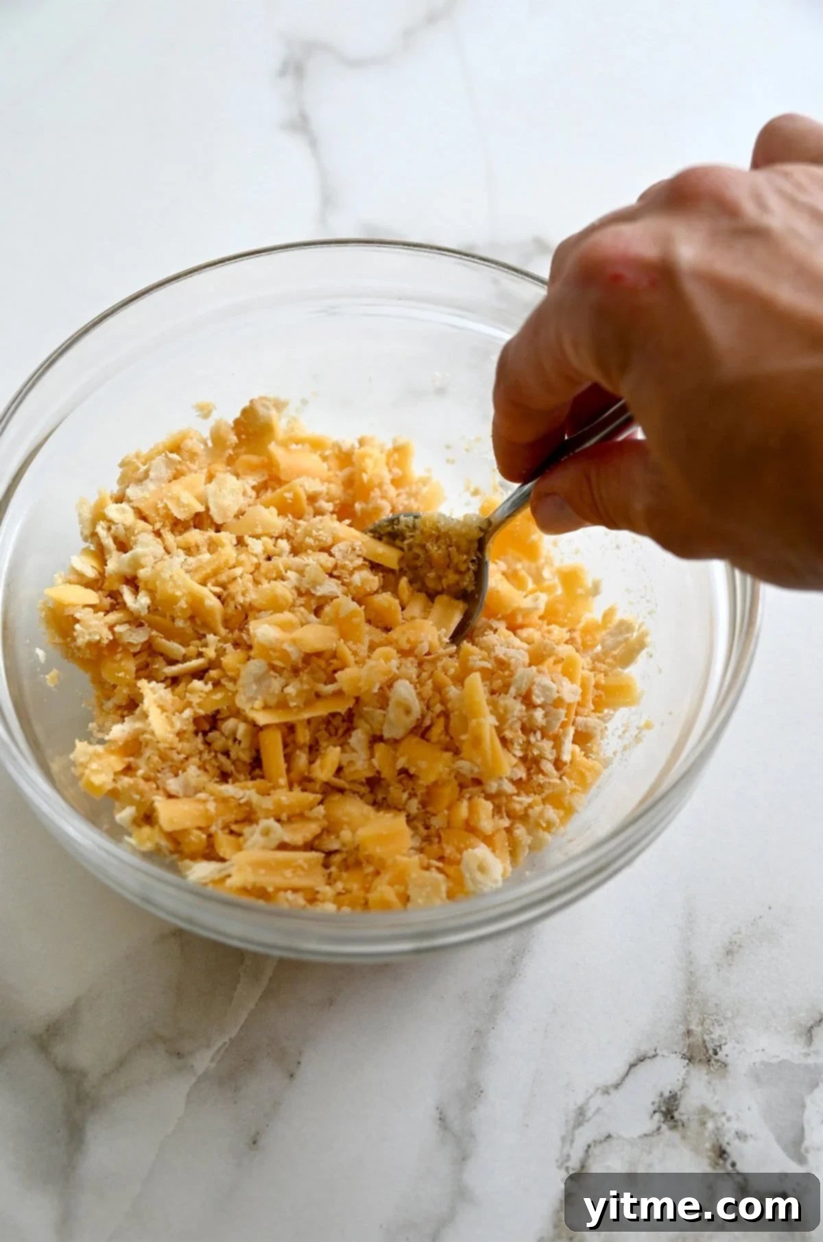 Crushed Ritz crackers being stirred together with melted butter and shredded cheddar.