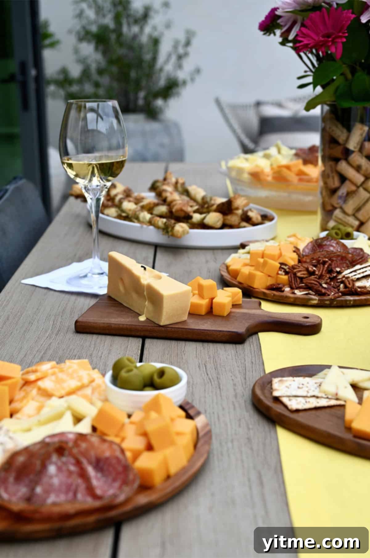 An opulent wine and cheese party spread artfully arranged on a rustic wooden table, featuring an abundant selection of assorted cheeses, crisp crackers, cured meats, vibrant fresh fruit, sweet jam, and elegant wine glasses, all complemented by decorative touches like charming small cheese boards and a whimsical cheese candle centerpiece.
